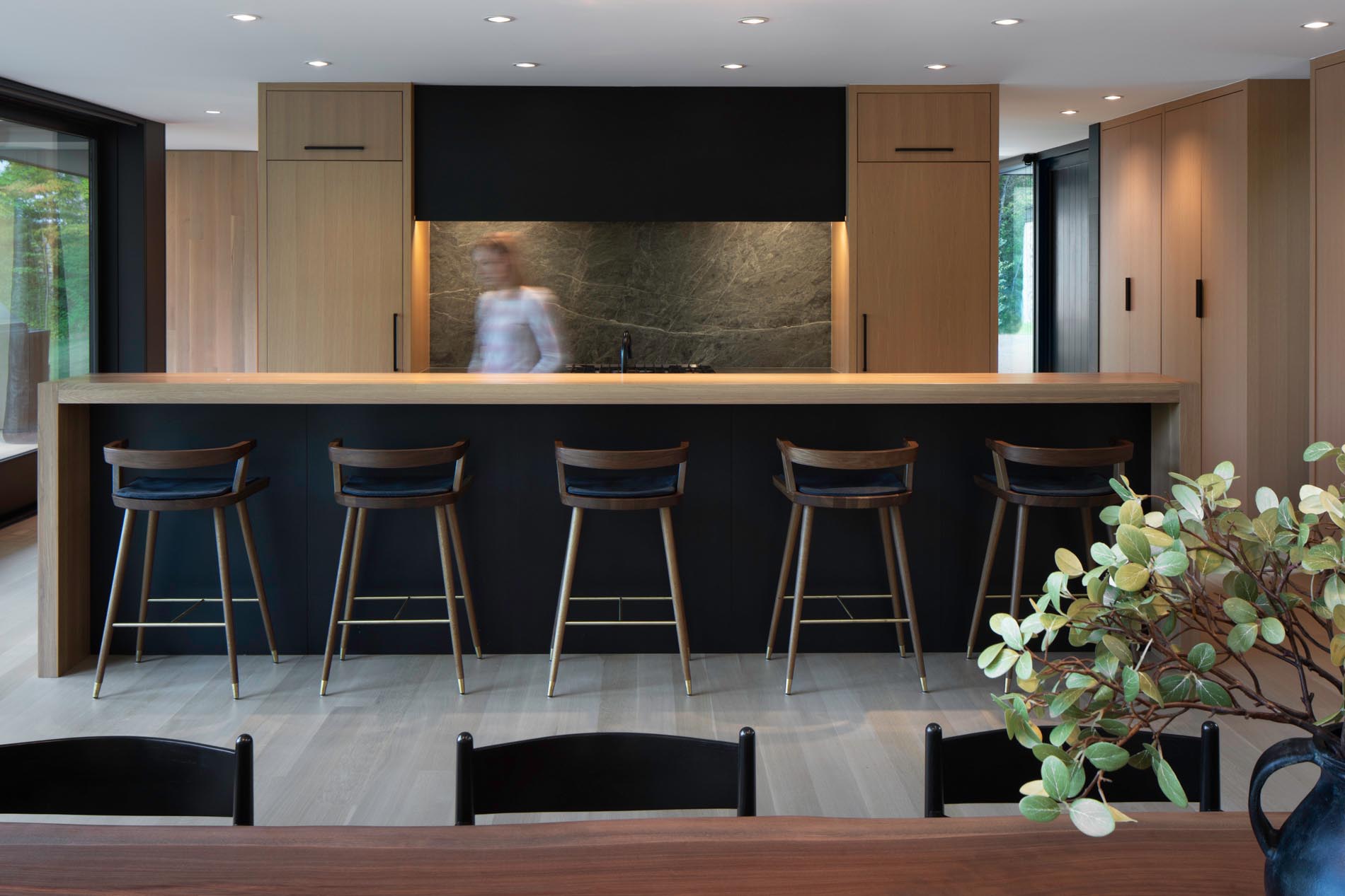 The design of the kitchen includes rift-sawn white oak cabinetry, a custom black metal hood, stone backsplash, and an island that's long enough to seat five.