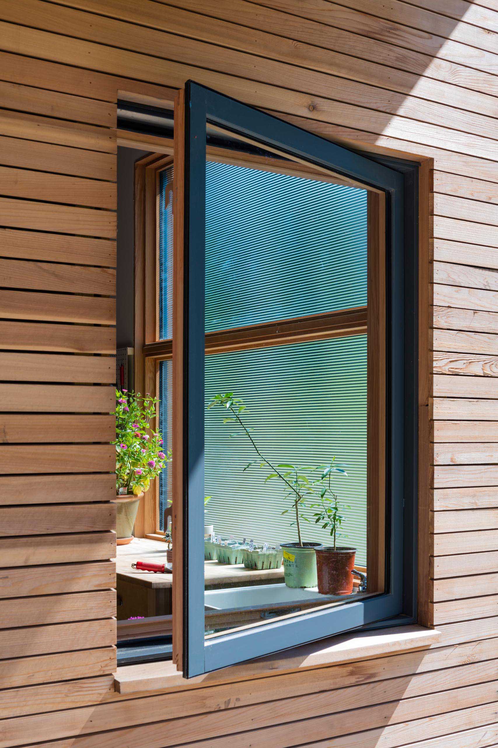 A deck wraps around this modern home, while the charcoal-colored window frames provide a contrast to the wood and complement the metal roof and garage door.