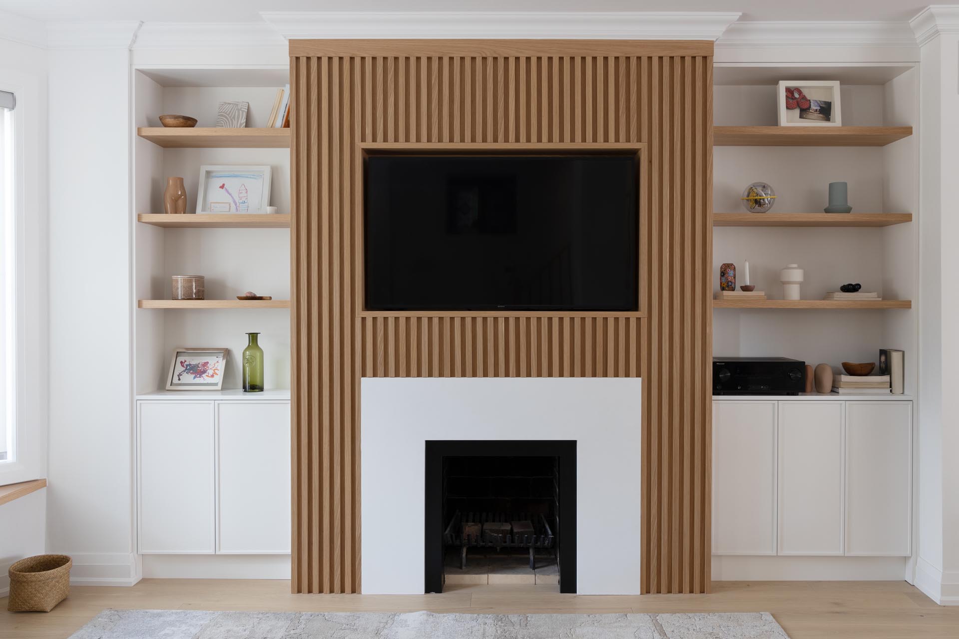 This living room wall has a Scandinavian-inspired design that includes a wood slatted wall that draws the eye, adds a sense of depth, and surrounds the television and fireplace.