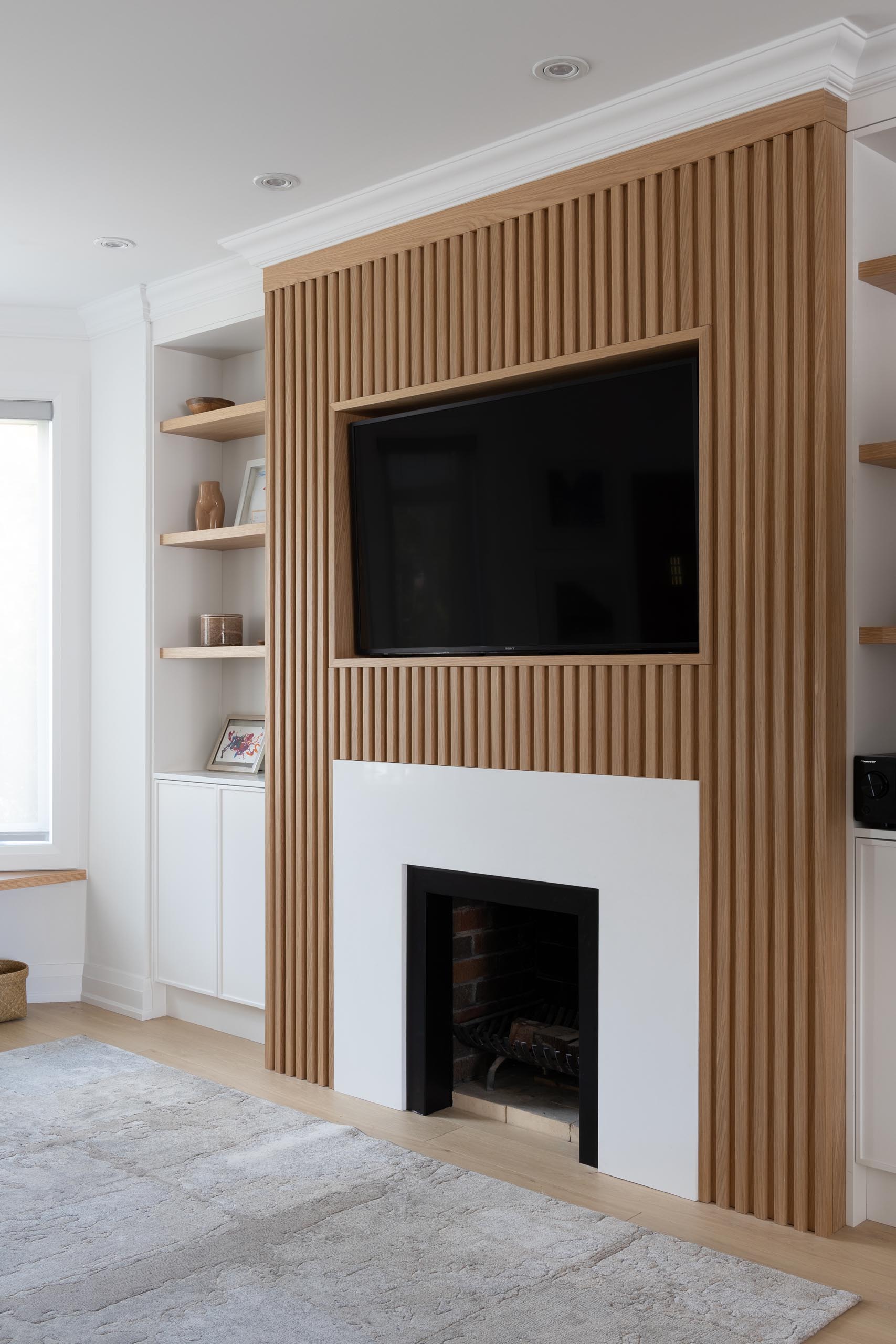 This living room wall has a Scandinavian-inspired design that includes a wood slatted wall that draws the eye, adds a sense of depth, and surrounds the television and fireplace.