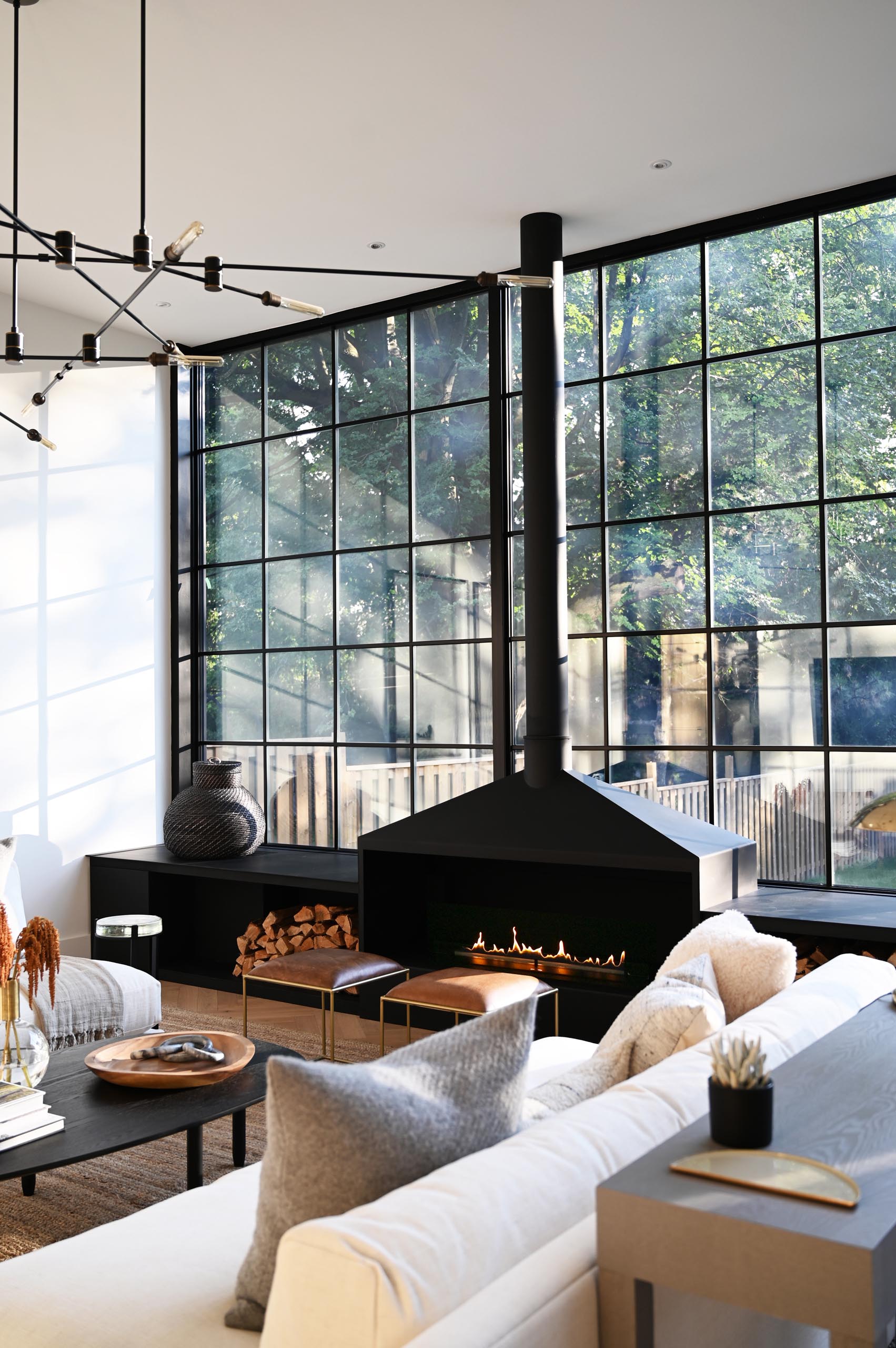 The expansive wall-to-wall black-framed windows and door frames complement the interior of the living room, that showcases a matte black fireplace and window bench. Also included in the design of the window bench is firewood storage.