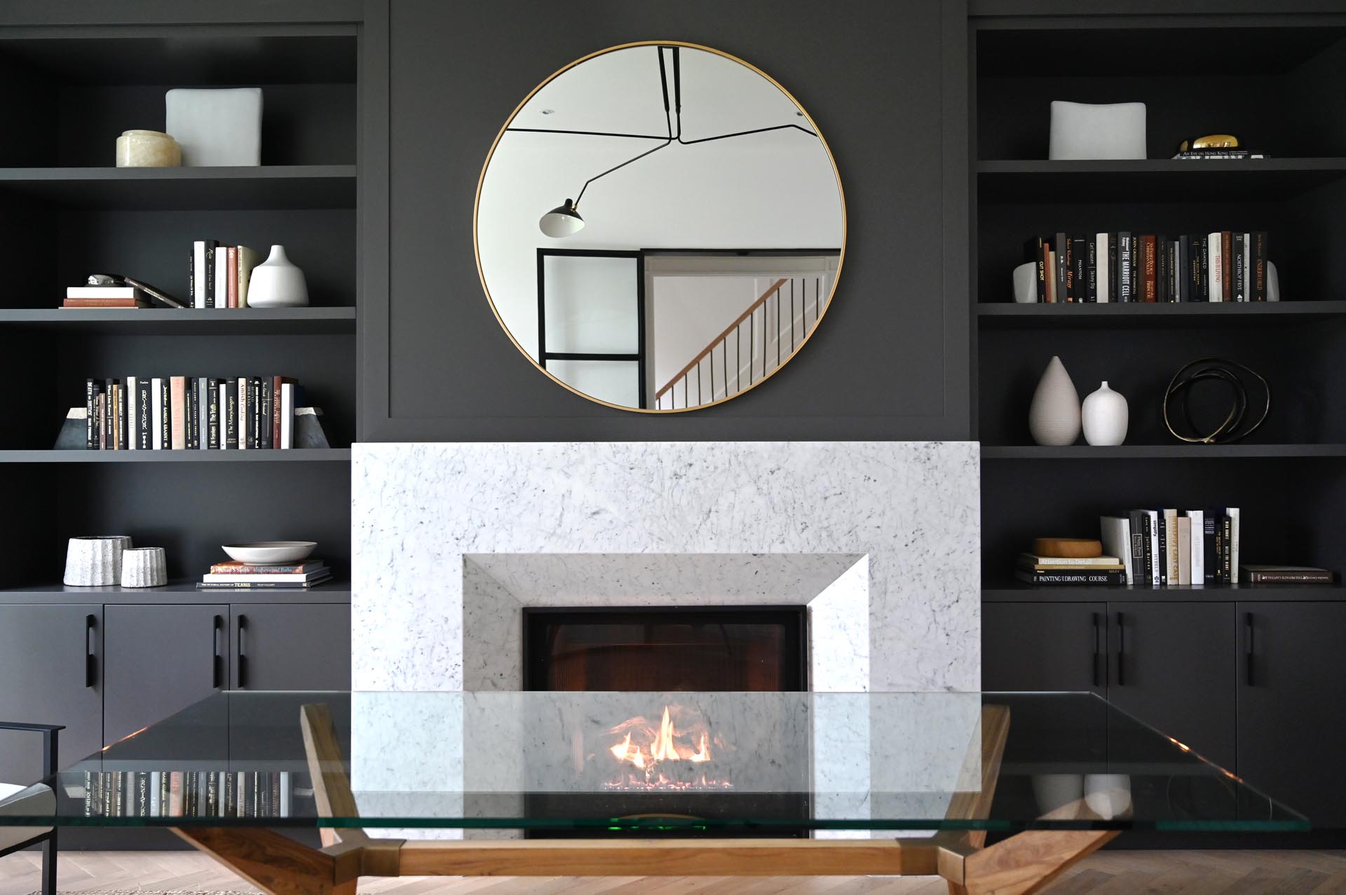 A modern home office has a black accent wall that provides a backdrop for the fireplace, while built-in shelving and cabinets add a storage element.