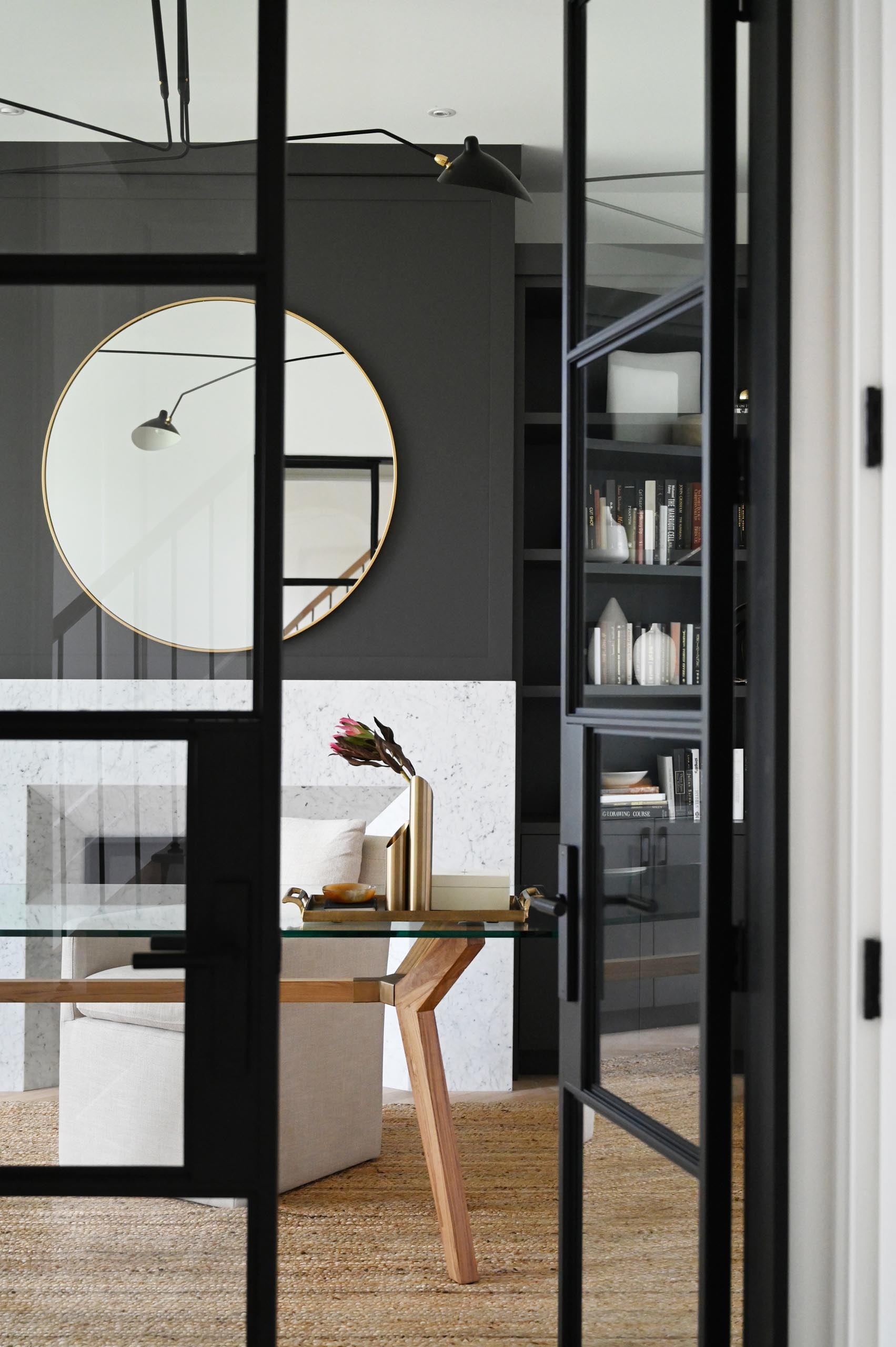 A modern home office has a black accent wall that provides a backdrop for the fireplace, while built-in shelving and cabinets add a storage element.