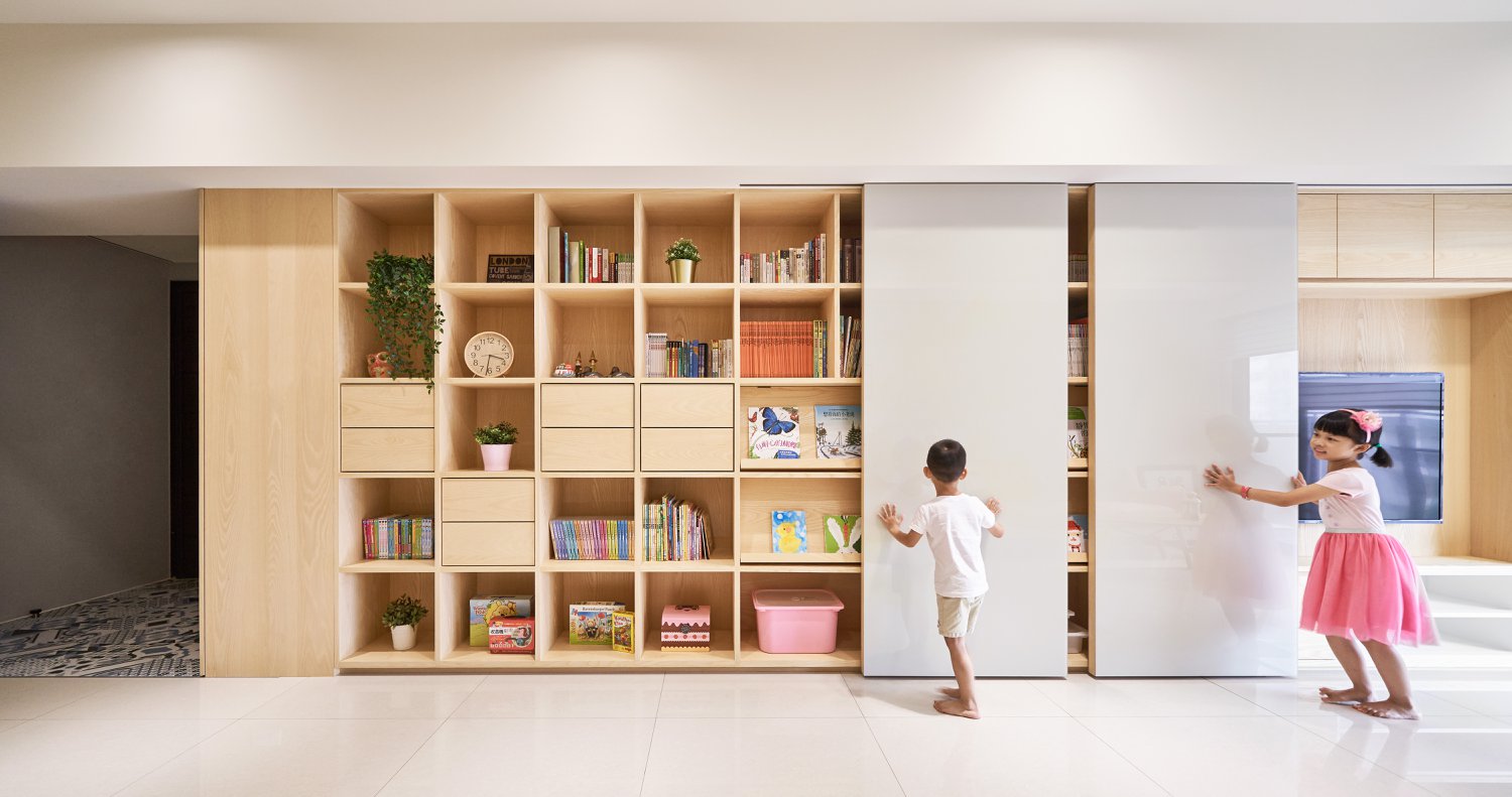 A modern shelving unit with open storage, drawers, book displays, whiteboard walls, and a hidden tv.