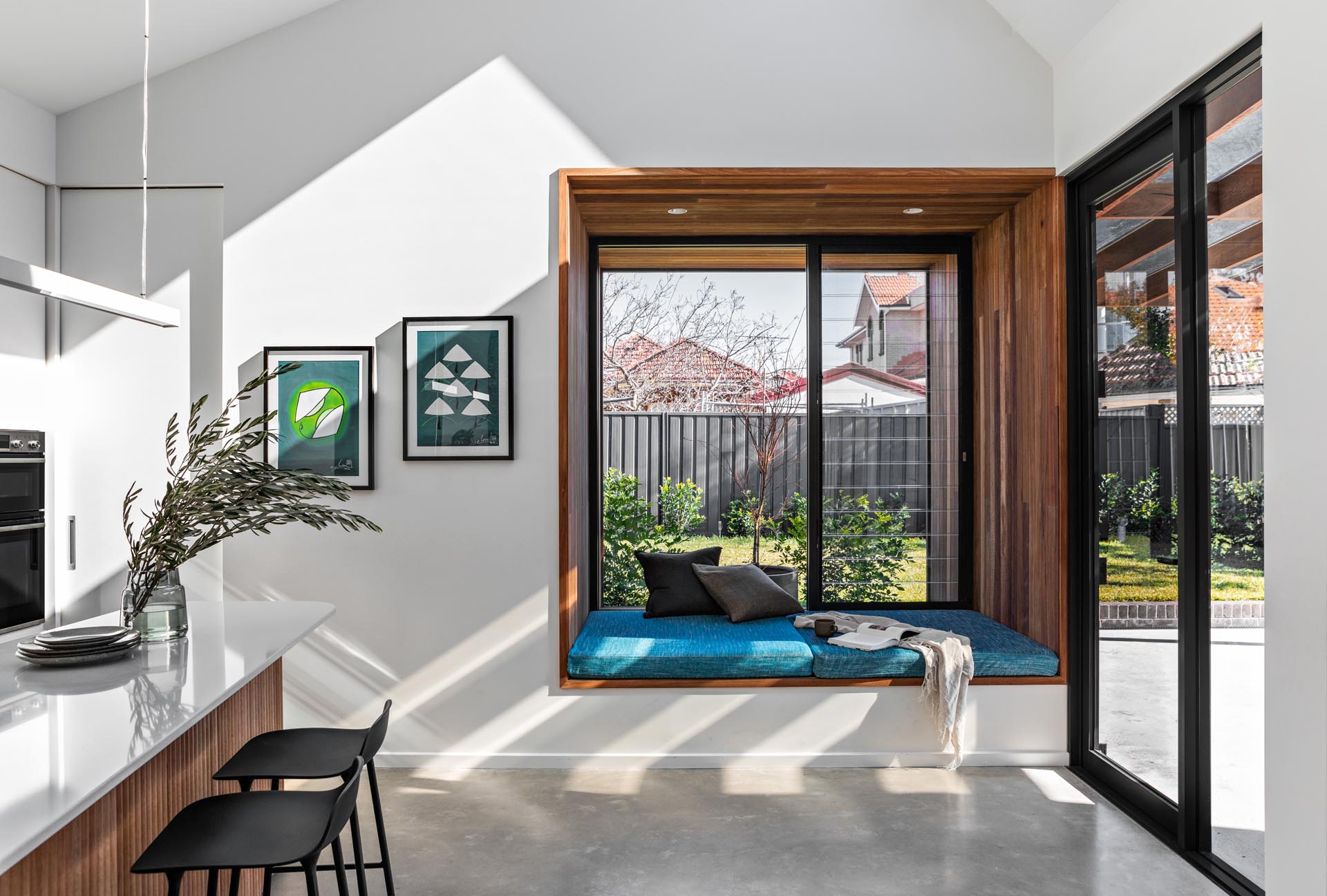 A large square timber-lined window box seat with blue upholstered cushion, that extends the view out to the garden.