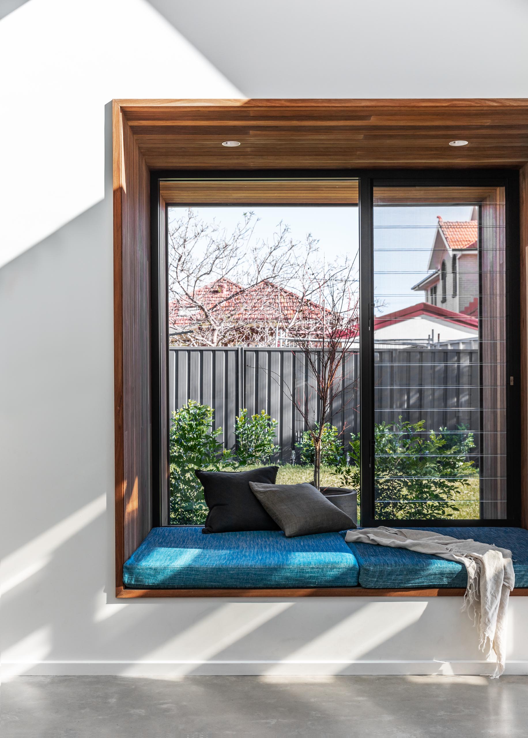 A large square timber-lined window box seat with blue upholstered cushion, that extends the view out to the garden.