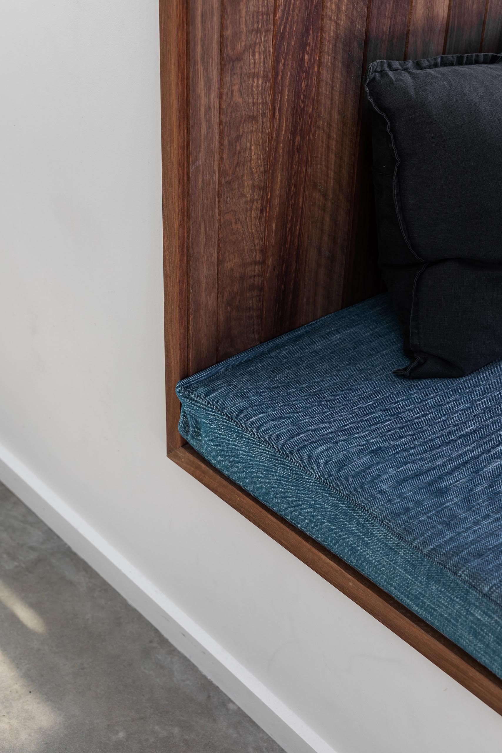 A large square timber-lined window box seat with blue upholstered cushion, that extends the view out to the garden.