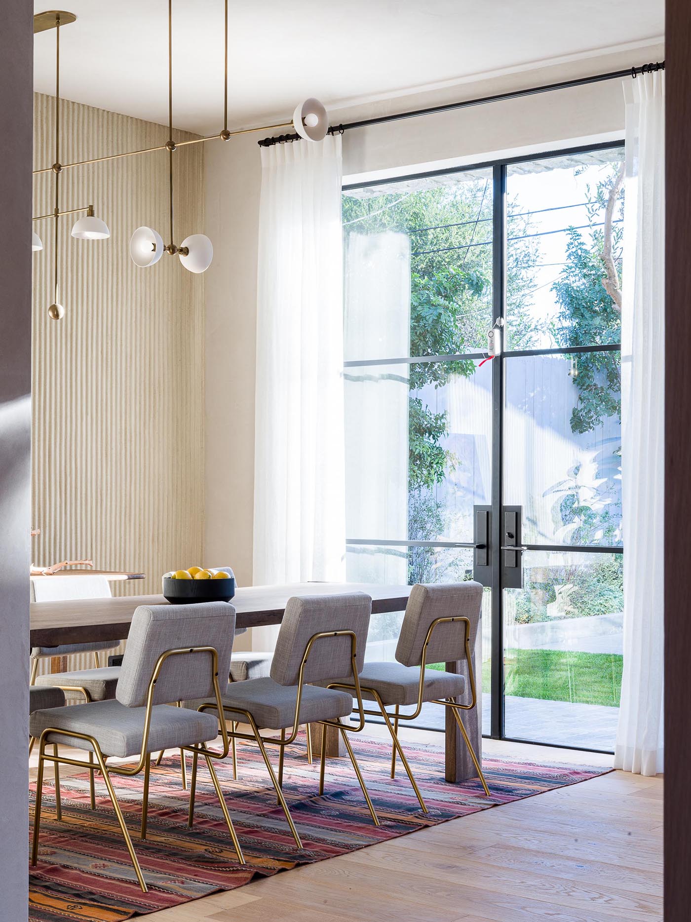 This modern formal dining area showcases a statement plaster wall, while black-framed glass doors open to the backyard.