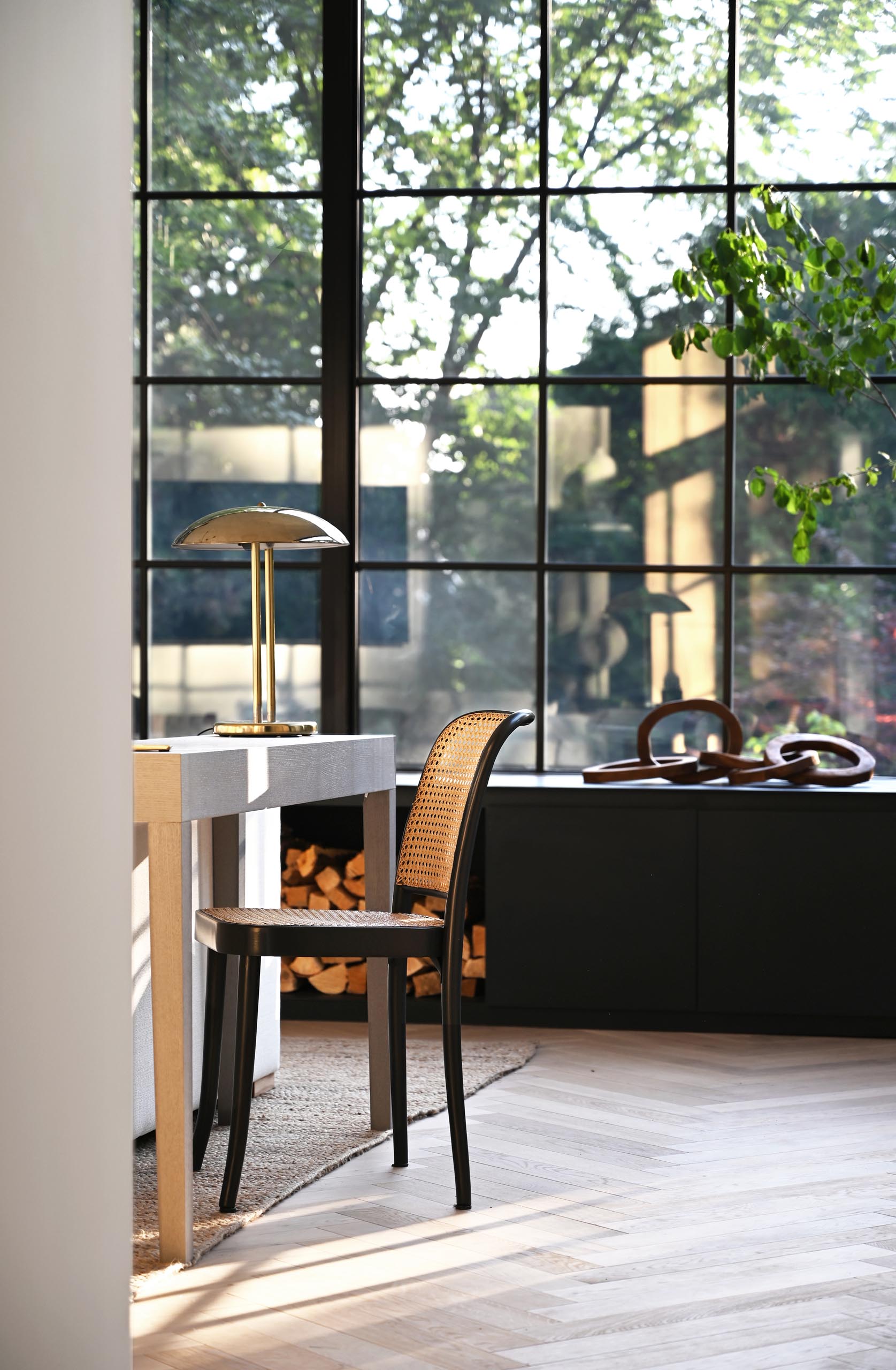 The expansive wall-to-wall black-framed windows and door frames complement the interior of the living room, that showcases a matte black fireplace and window bench. Also included in the design of the window bench is firewood storage.