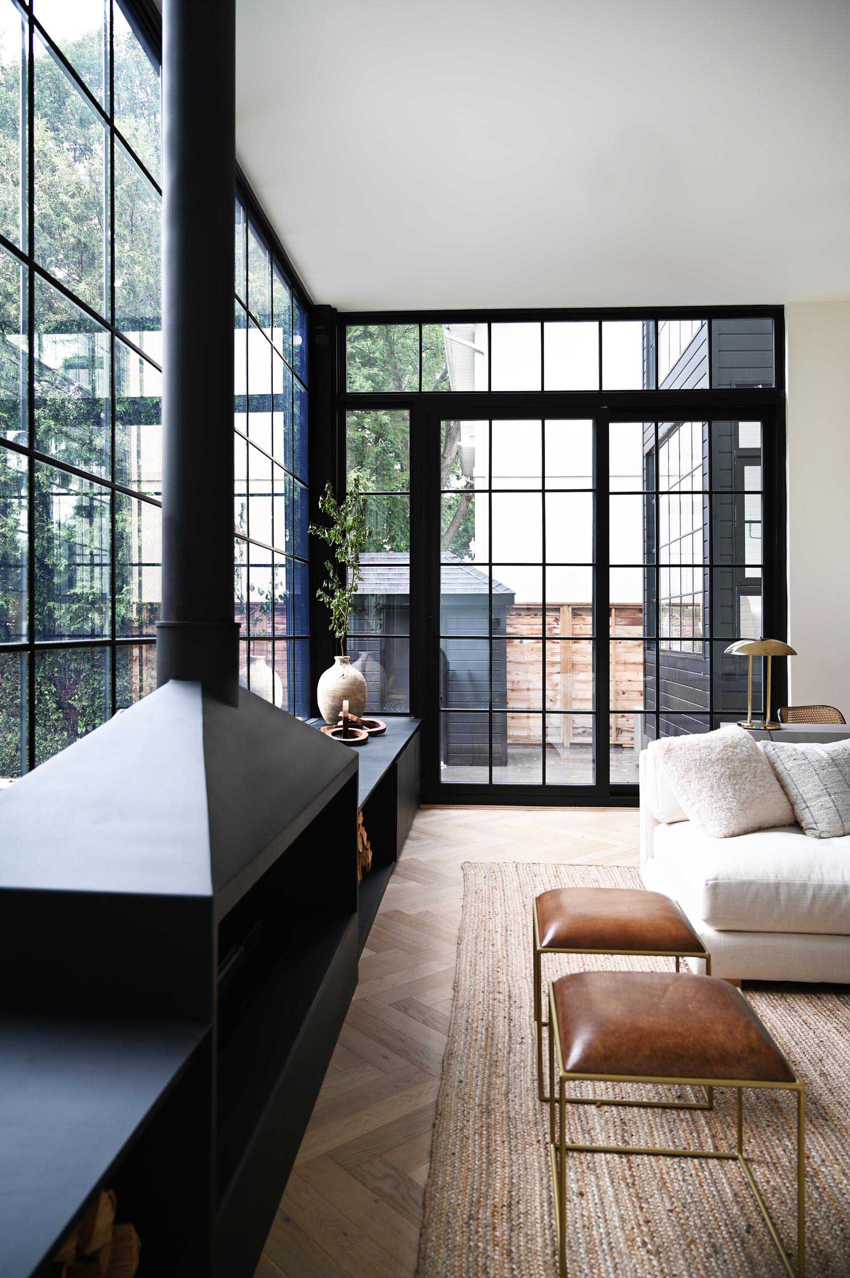 The expansive wall-to-wall black-framed windows and door frames complement the interior of the living room, that showcases a matte black fireplace and window bench. Also included in the design of the window bench is firewood storage.