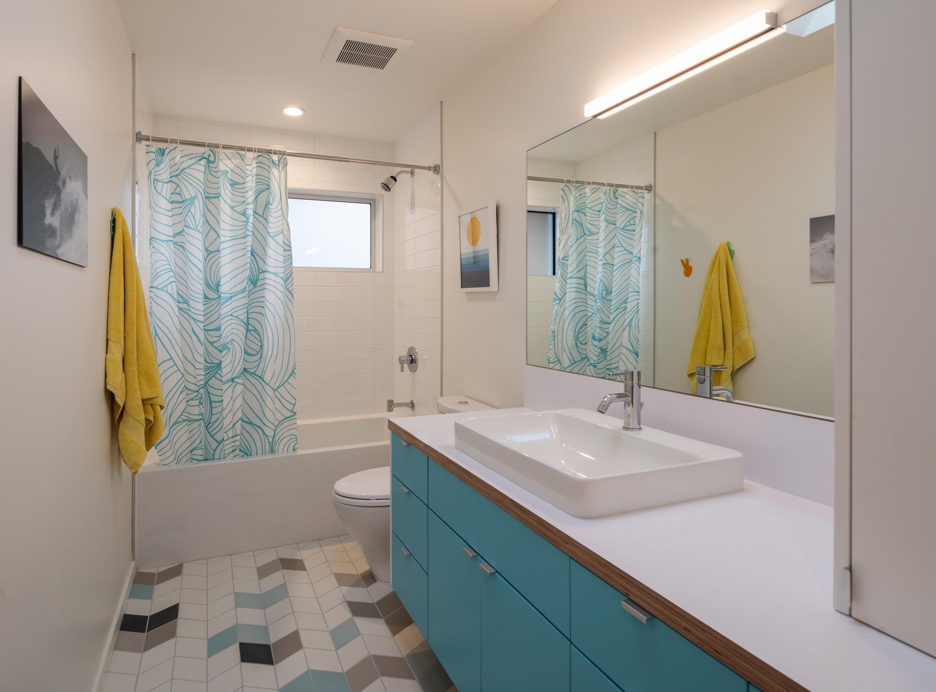 In this bathroom, a bright blue vanity is topped with a white countertop, while the chevron floor tiles feature a few different colors adding interest to the room.