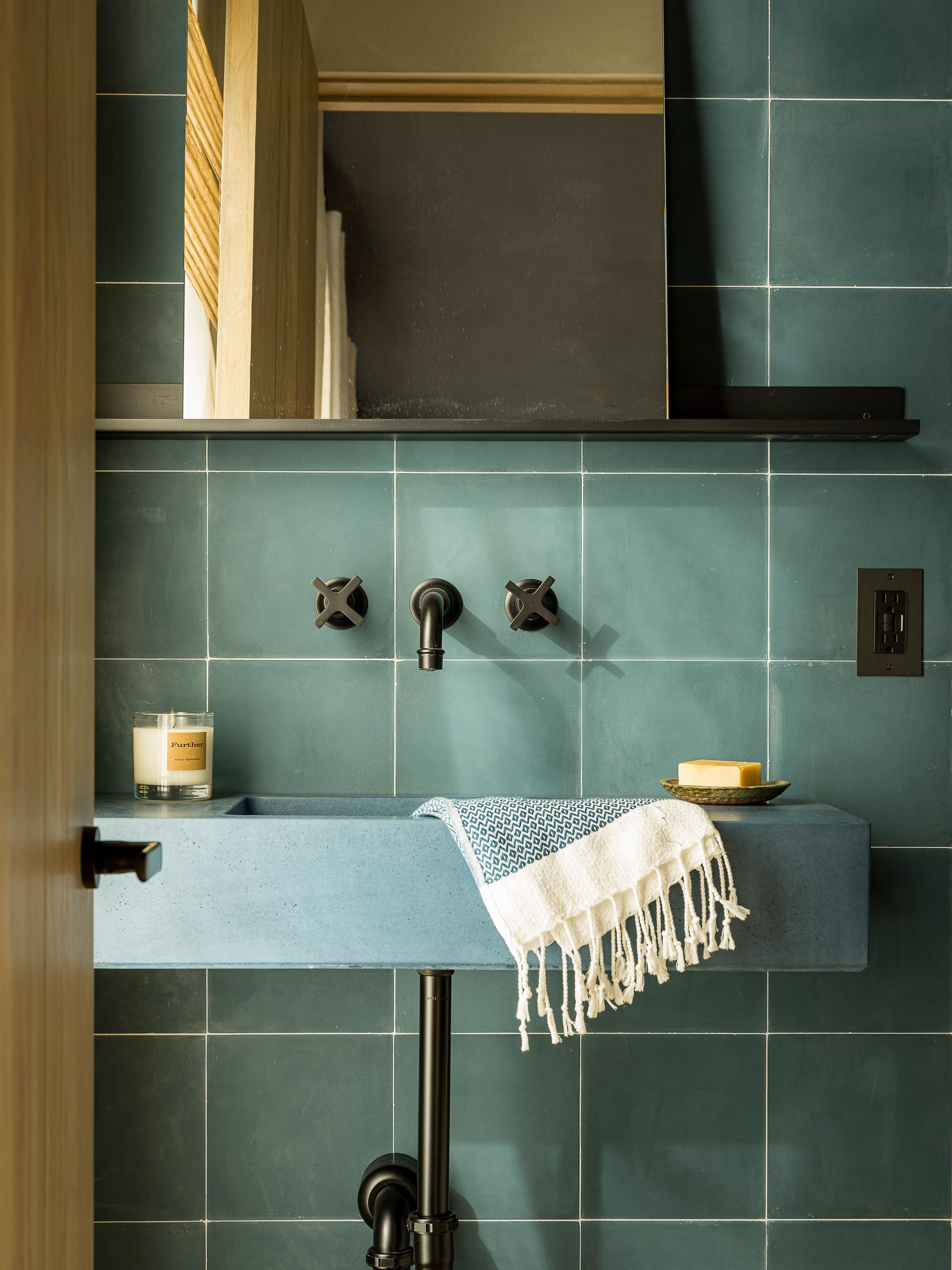 A contemporary blue-green bathroom with square tiles, a blue sink, and black hardware.