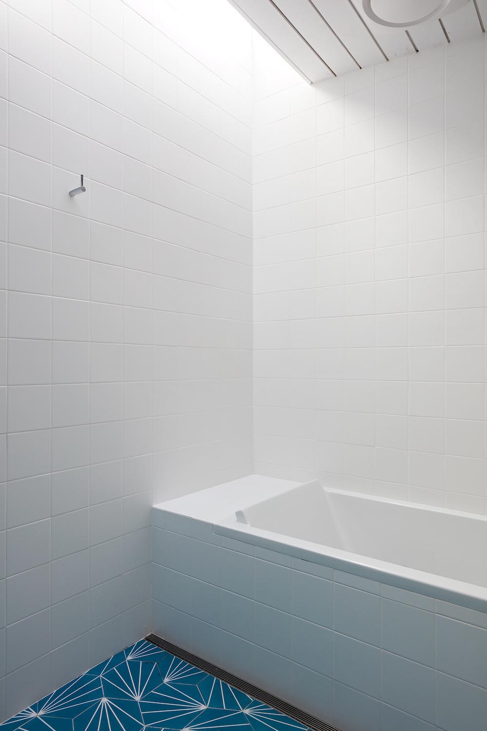 A modern white bathroom with blue starburst tiles and a built-in bathtub.