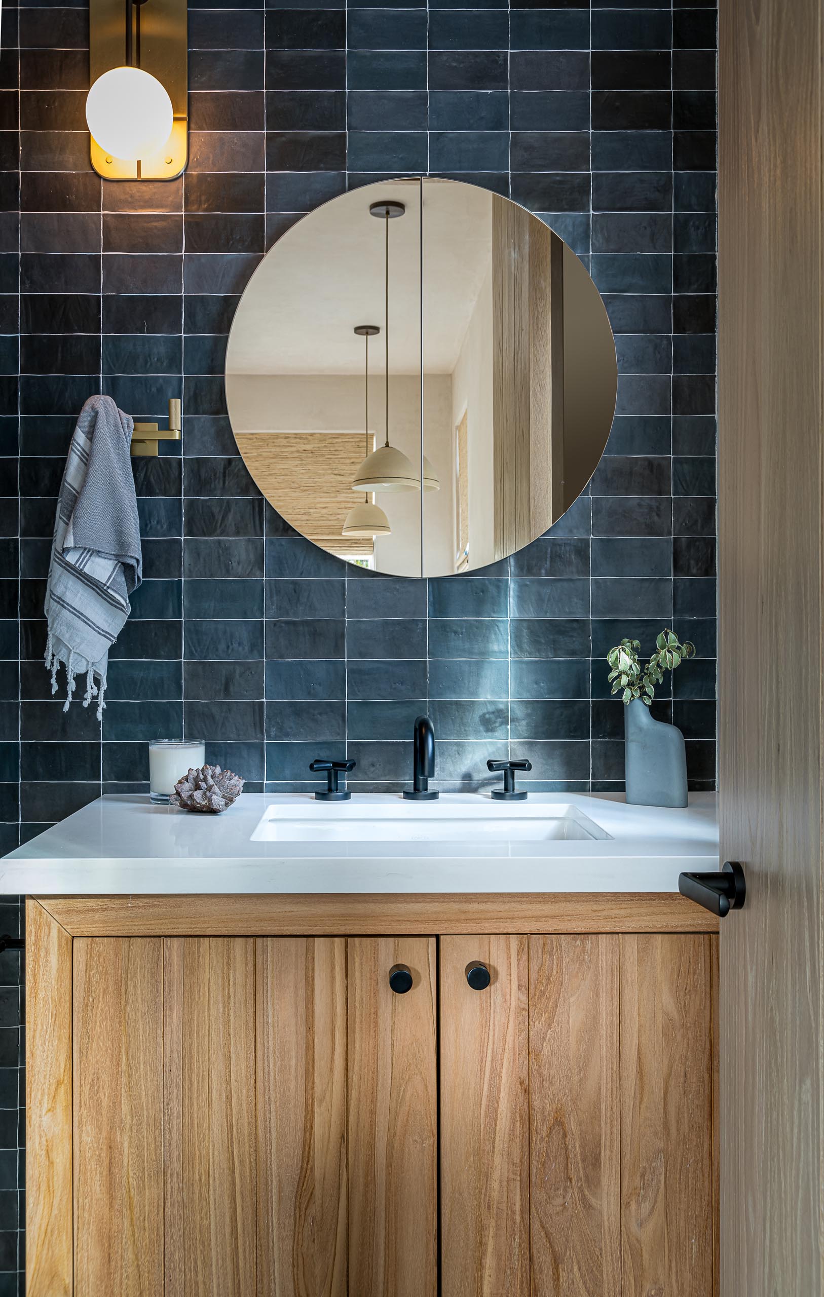 A contemporary bathroom with textured blue tiles, a wood vanity with white sink and countertop, and a round mirror.