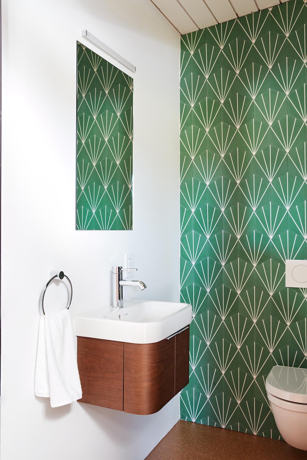 A modern white bathroom with green starburst tiles and a wood vanity.
