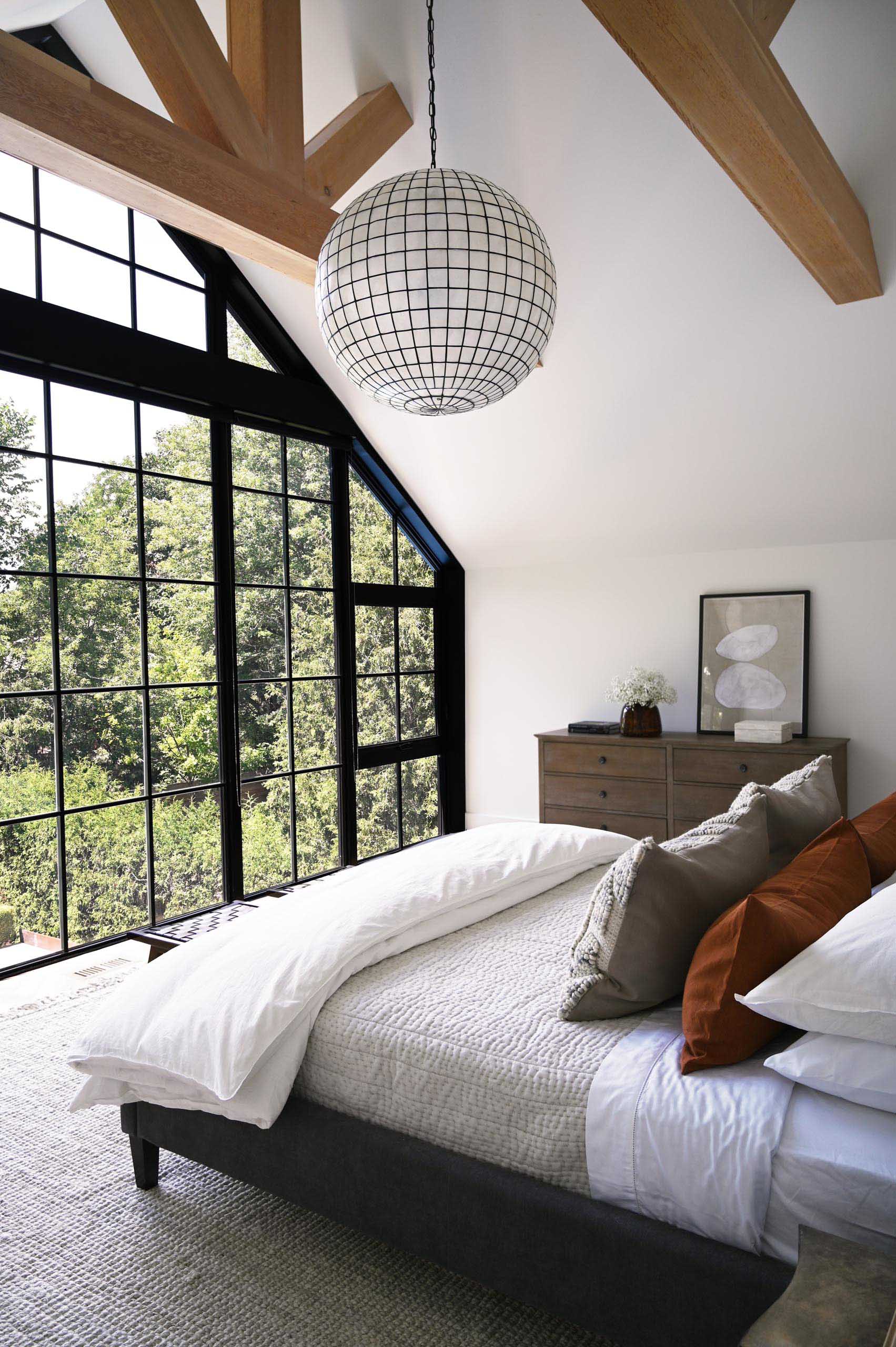 In this modern primary bathroom, one entire wall is dedicated to the black framed windows, flooding the room with natural light and creating a contrasting design element to the white walls and wood beams.