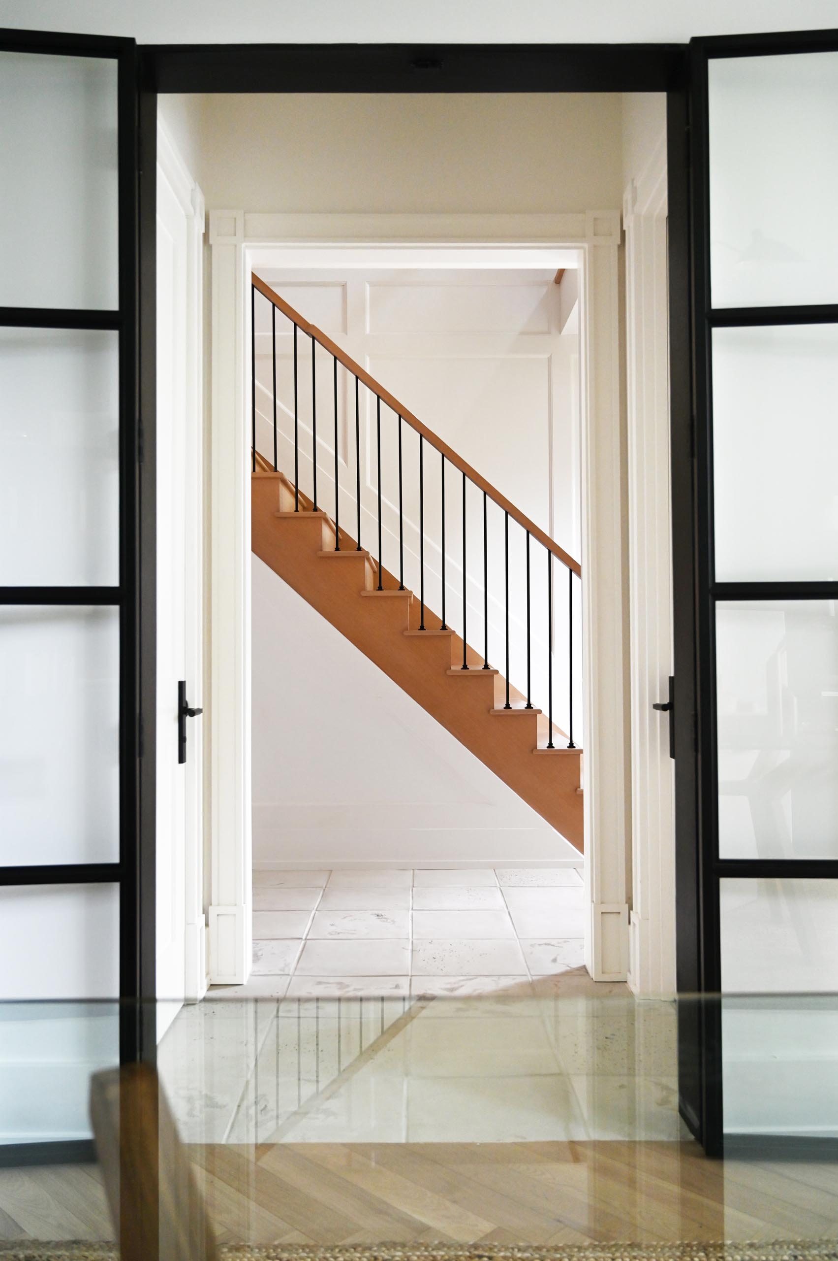 Black metal stair pickets and feature wall paneling, lead up to the second floor, where one is met with a catwalk overlooking the dining and kitchen space below.