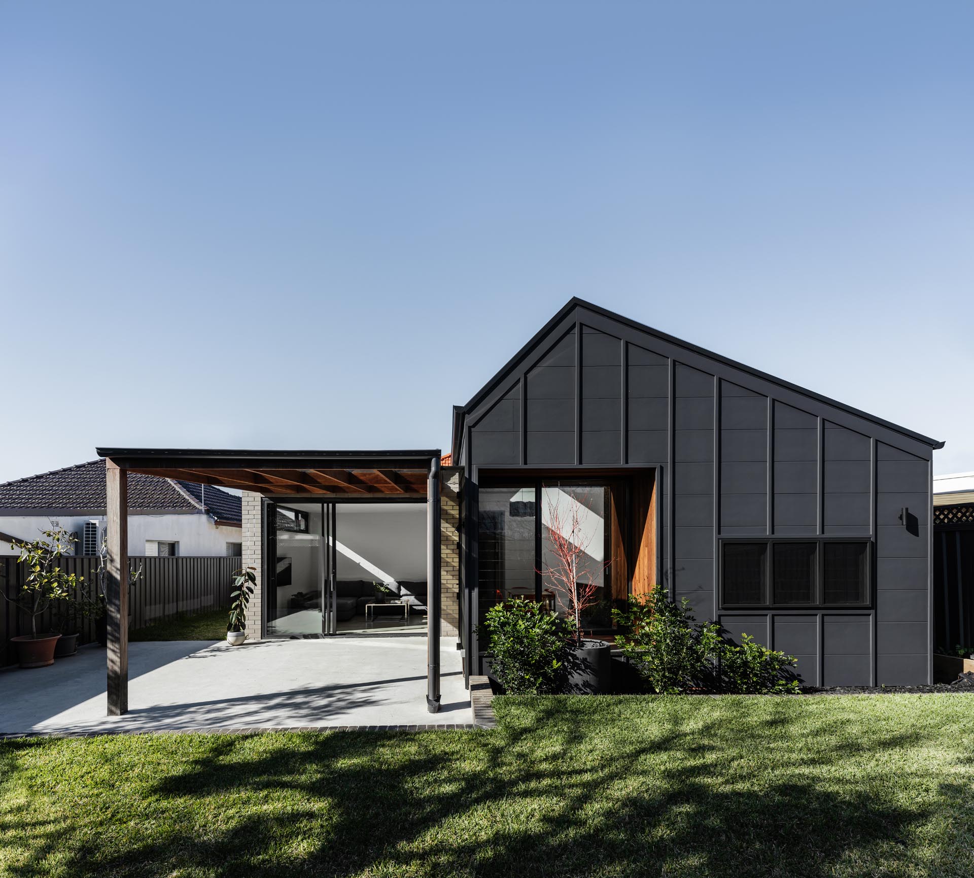 A simplified rear addition with a black and brick exterior includes a kitchen, dining, and living room with an improved connection to the outdoors via a covered patio.