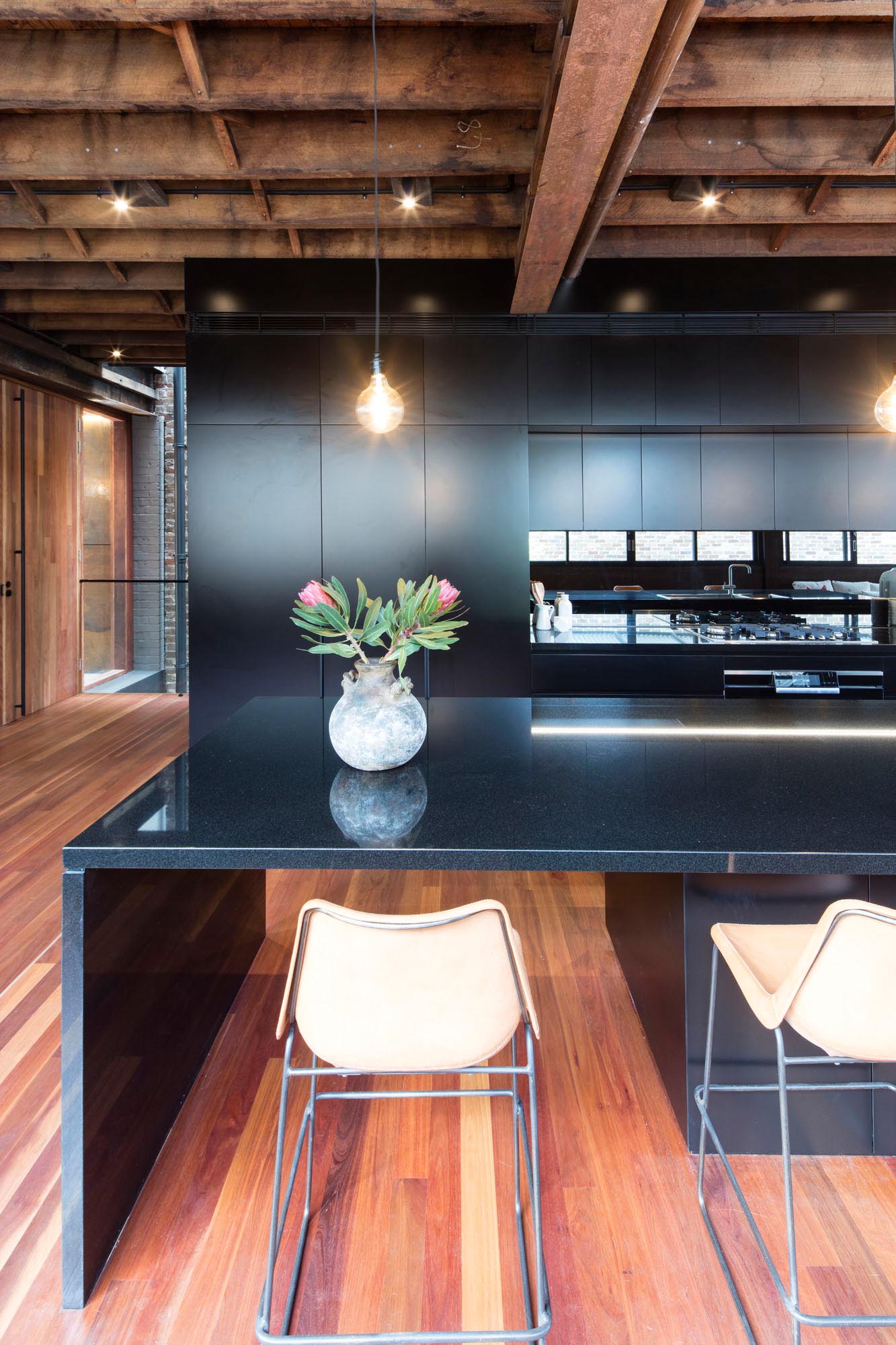 The kitchen, which separates the living room from the dining area and courtyard, has matte black cabinets, black countertops, a mirrored backsplash, and a long island.