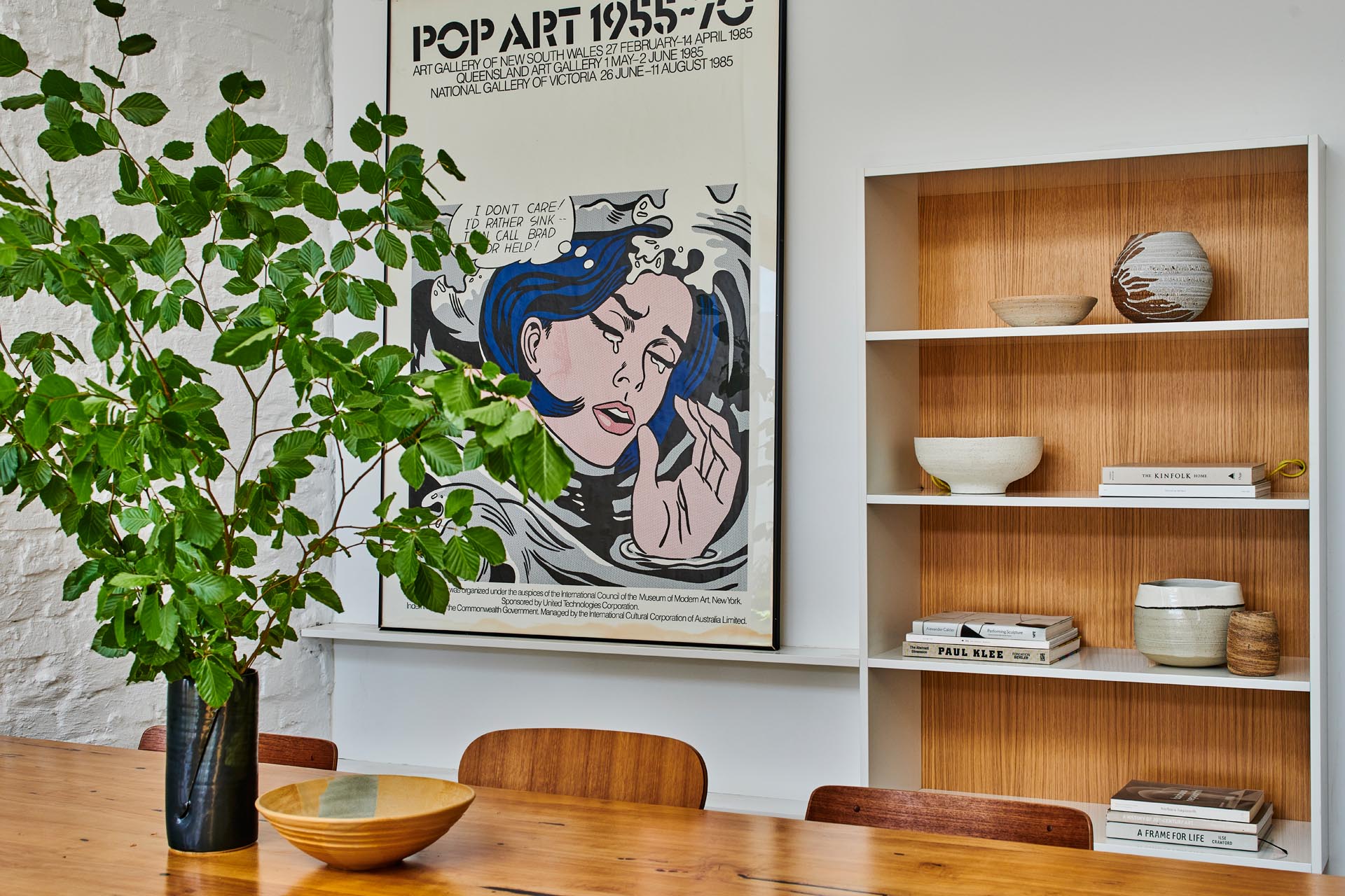 In this modern dining area, there's a bookshelf that's partially set back into the wall. The wood backing allows the decorative items to stand out.