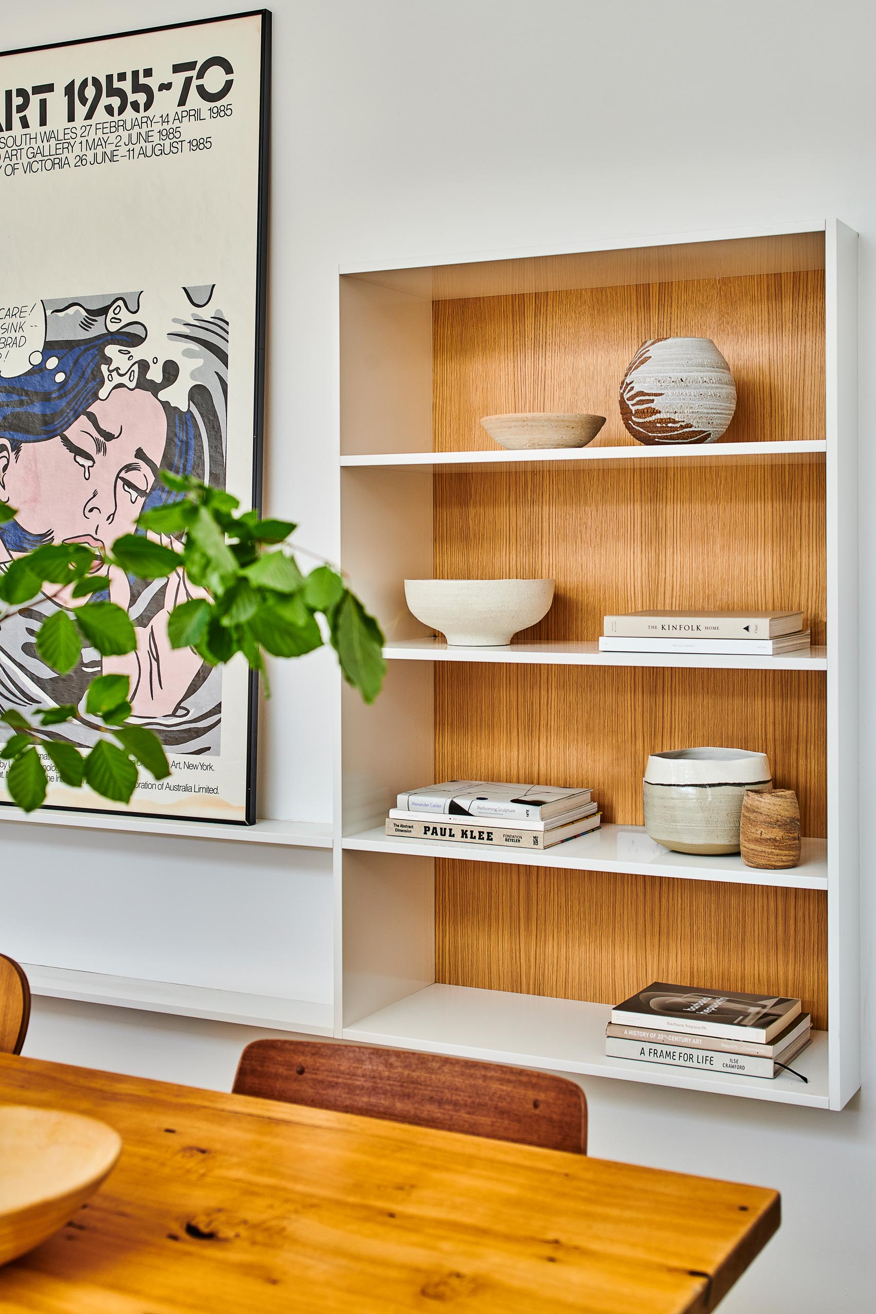 In this modern dining area, there's a bookshelf that's partially set back into the wall. The wood backing allows the decorative items to stand out.