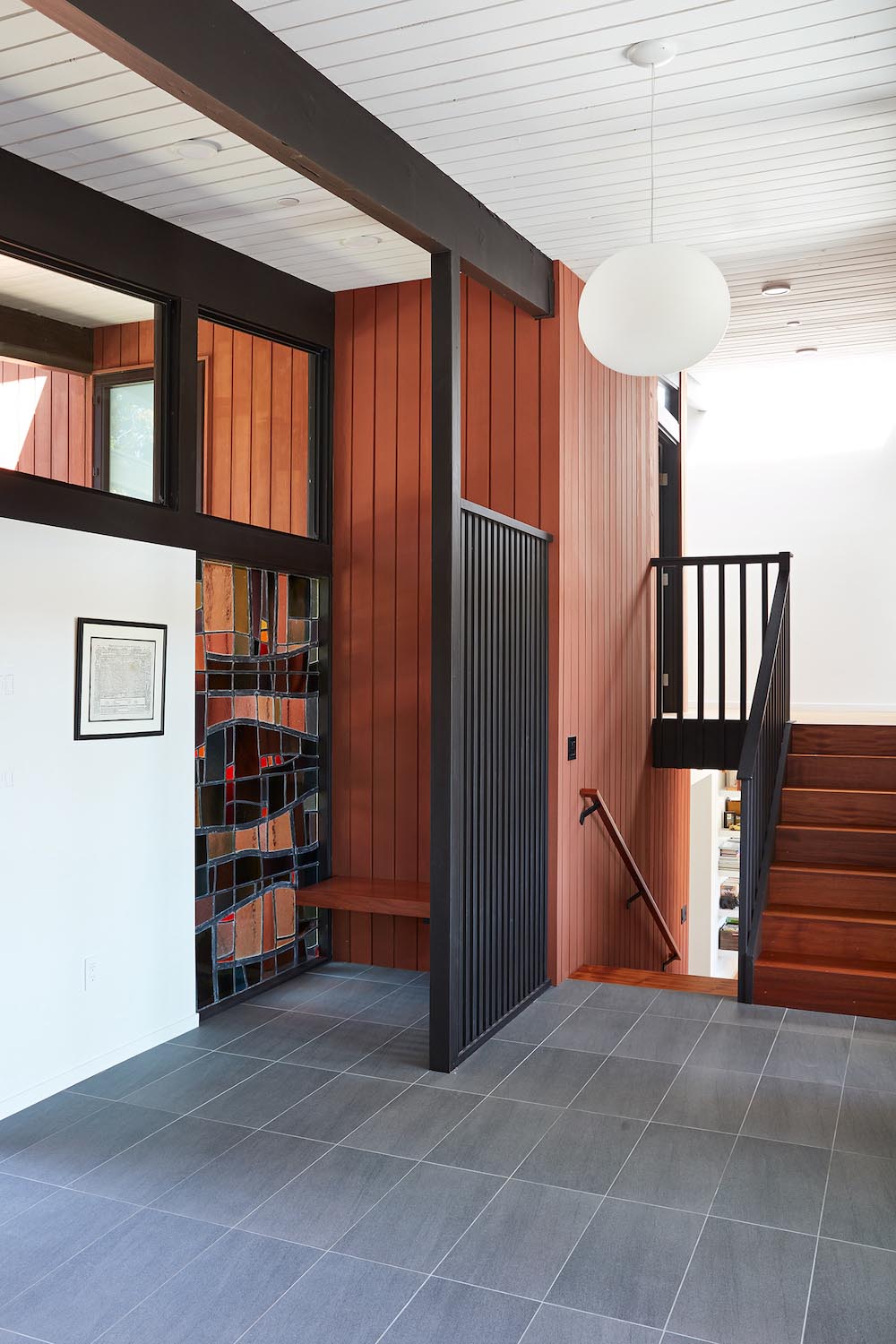 A remodeled entryway with gray floor tiles and an original stained glass window.