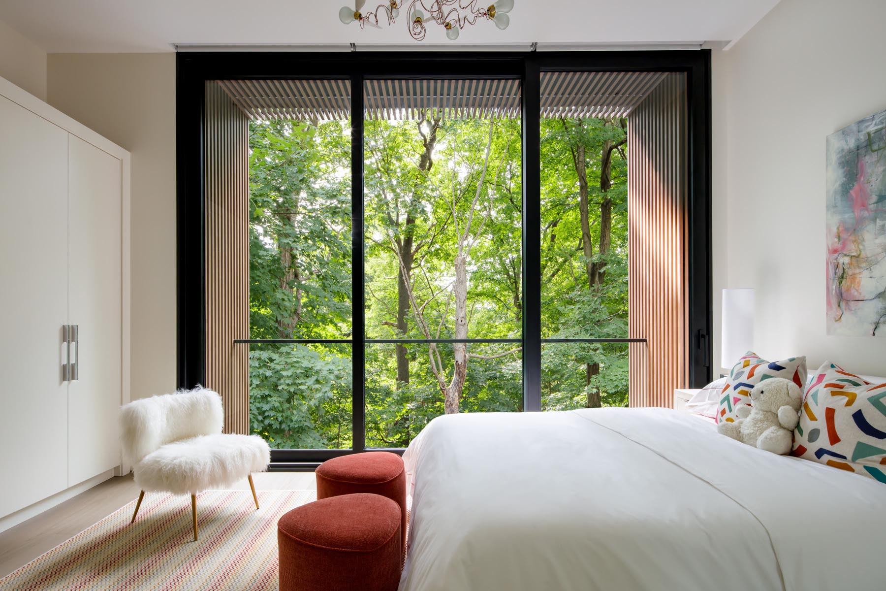 A modern bedroom with a glass door that opens to a small balcony with tree views.