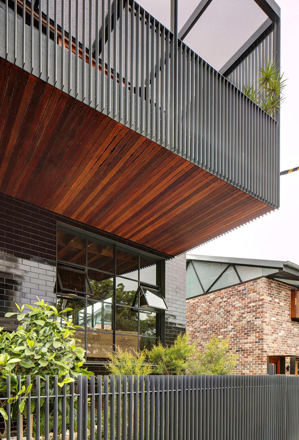 This modern home showcases a facade of glazed black tiles providing a new sophisticated exterior provides a backdrop for the landscaping, which includes a lush urban garden and a small pond.