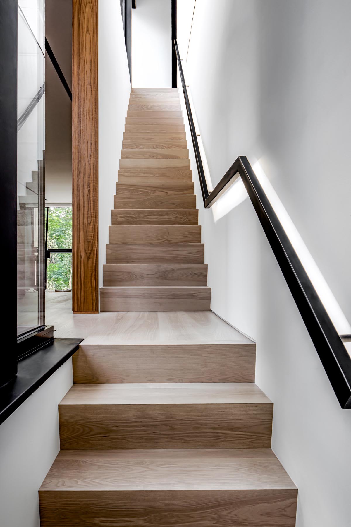 Wood stairs connect the various levels of this modern home, with a black handrail that contrasts the white wall.