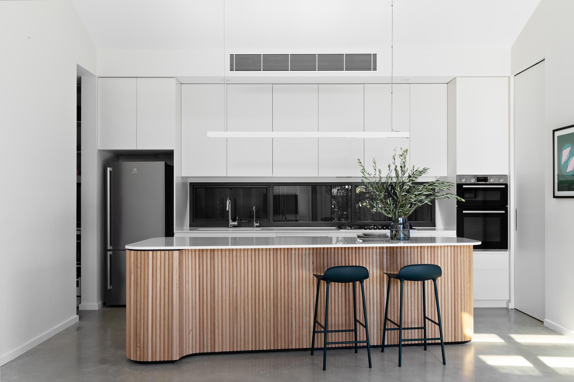 In this modern kitchen, there's minimalist white cabinets, concrete floors, a glass backsplash, and an island with wood facade.