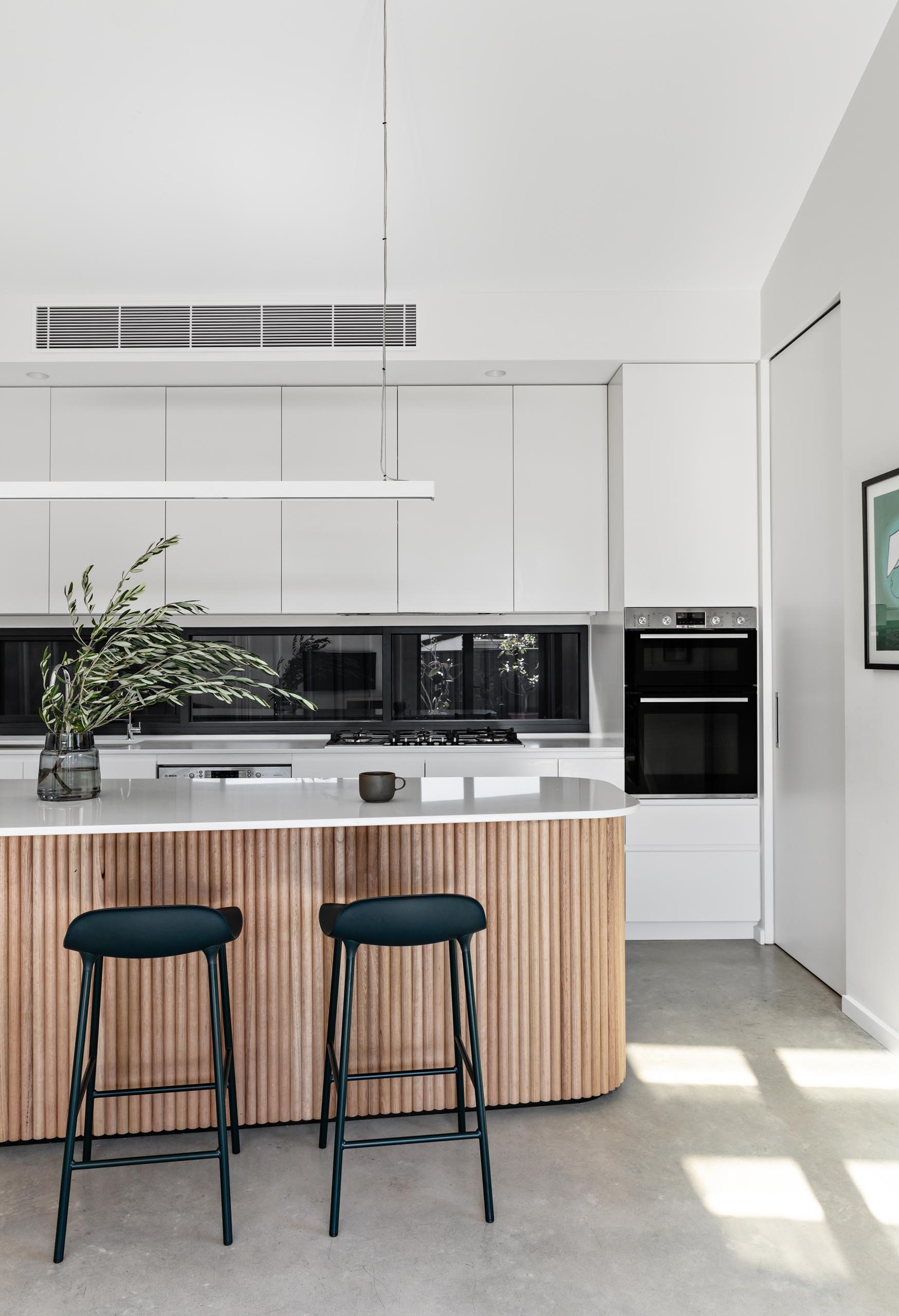 In this modern kitchen, there's minimalist white cabinets, concrete floors, a glass backsplash, and an island with wood facade.