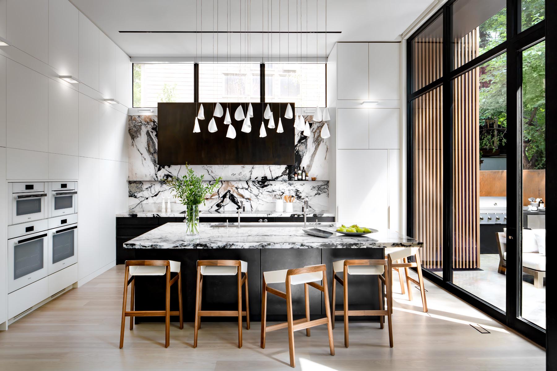 In this kitchen, minimalist white cabinets line the walls, while a large island provides space for multiple stools. Hidden within the cabinetry is a dedicated coffee station.