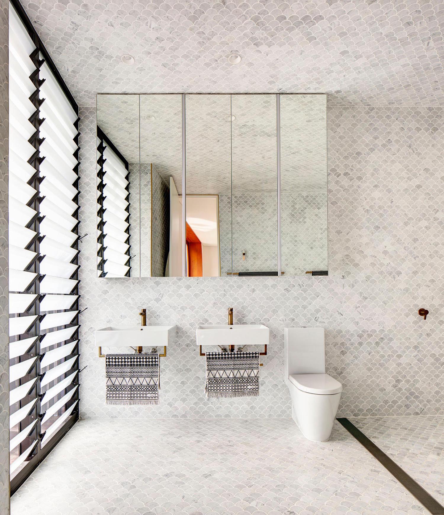 This modern en-suite master bathroom has the ceiling and tall walls clad with light grey fan tiles which compliment the brass fixtures