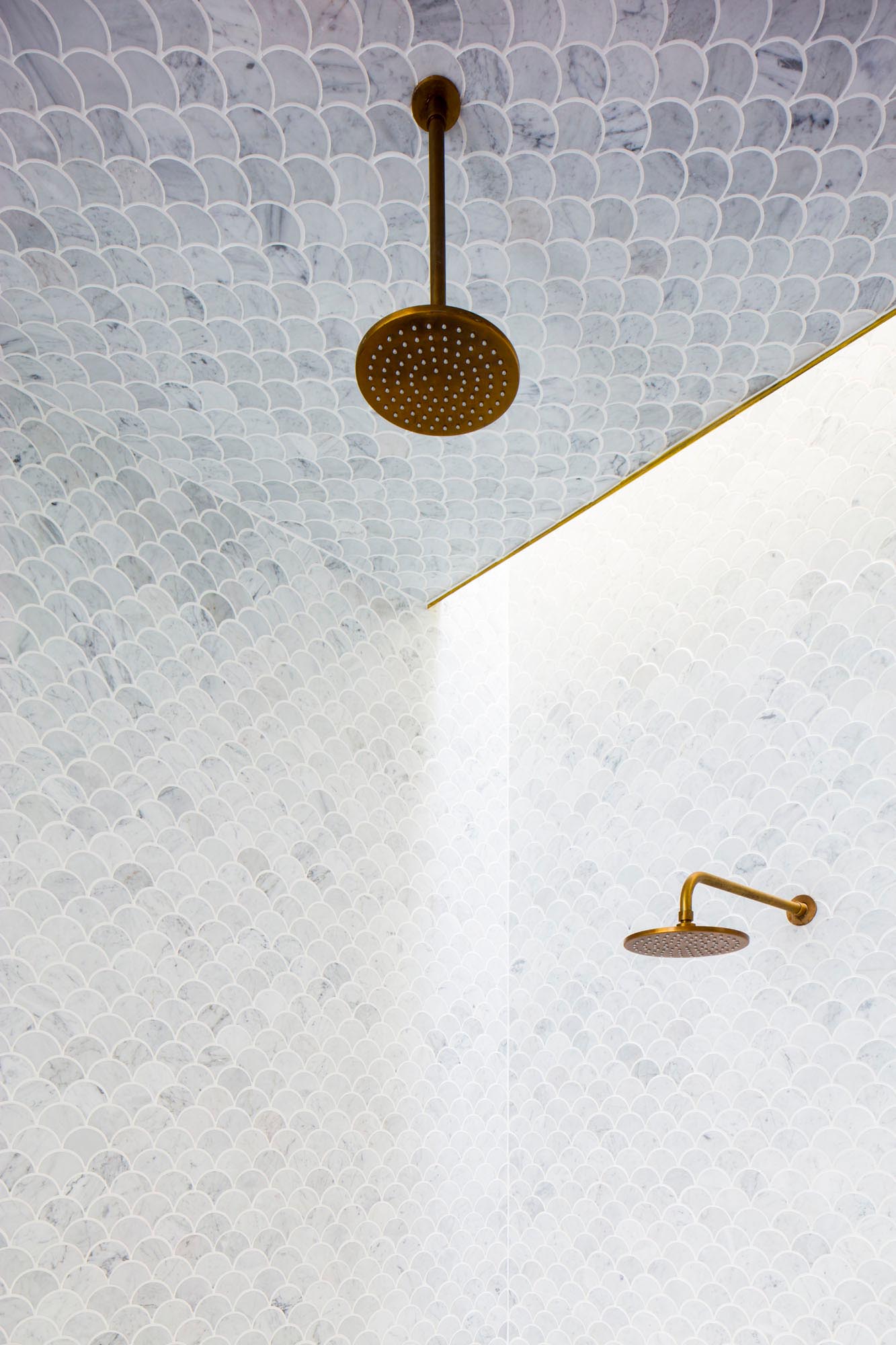 This modern en-suite master bathroom has the ceiling and tall walls clad with light grey fan tiles which compliment the brass fixtures