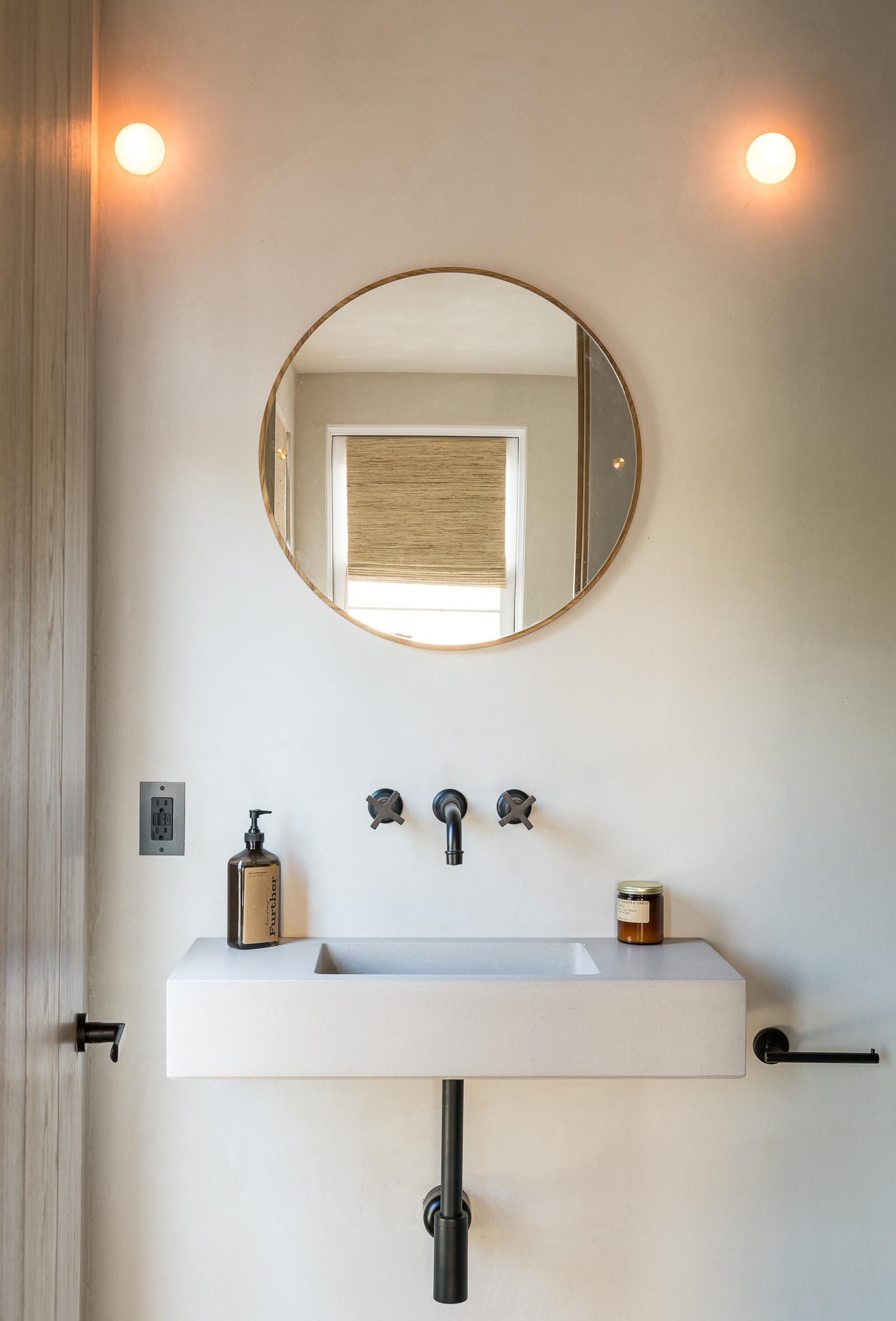 A minimalist bathroom sink with a round mirror and black hardware.