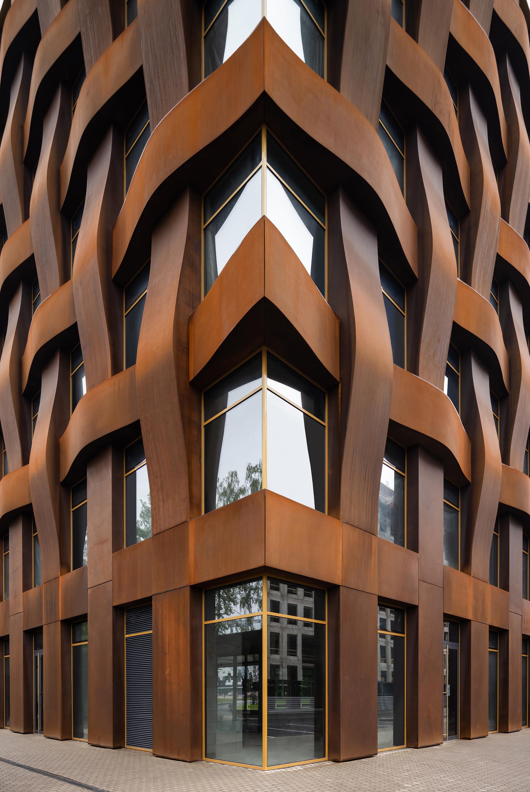 The sculptural weathered steel facade of this modern office building is constructed in a geometric grid and presents itself as a dynamic, organically flowing fabric of loose "warp and weft" threads.