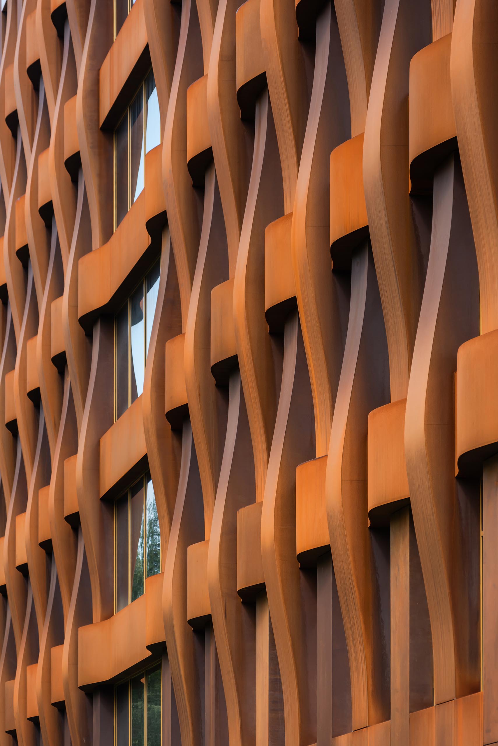 The sculptural weathered steel facade of this modern office building is constructed in a geometric grid and presents itself as a dynamic, organically flowing fabric of loose "warp and weft" threads.