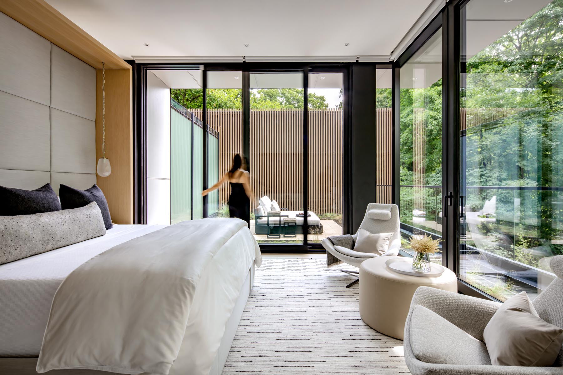This modern primary bedroom has floor-to-ceiling windows, and a sliding glass opens to a private outdoor space.