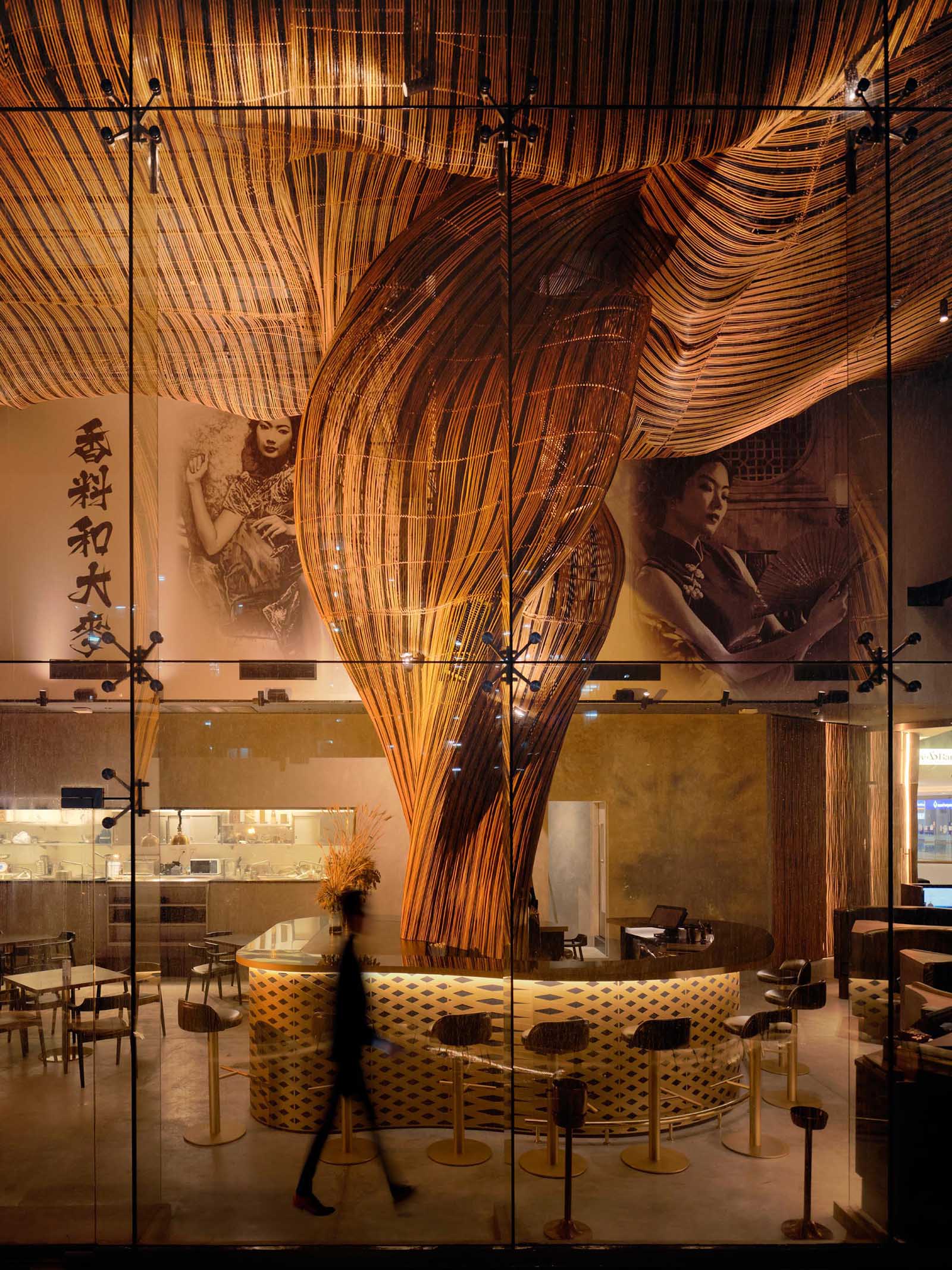 A modern restaurant with a glass facade that showcases flowing rattan sculptures inside.