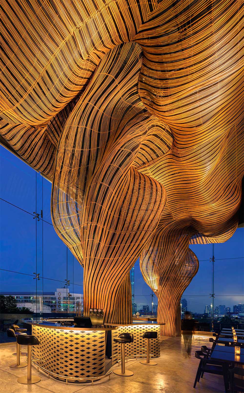 A modern restaurant with a glass facade that showcases flowing rattan sculptures inside.