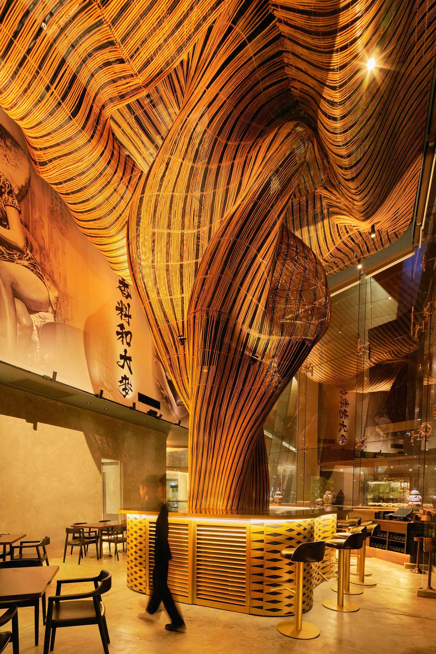 A modern restaurant with a glass facade that showcases flowing rattan sculptures inside.