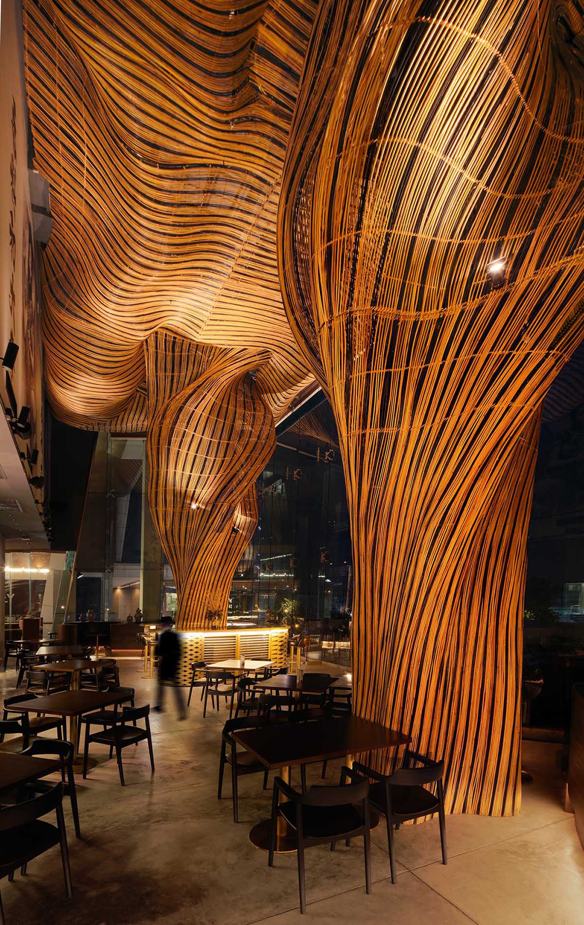 A modern restaurant with a glass facade that showcases flowing rattan sculptures inside.