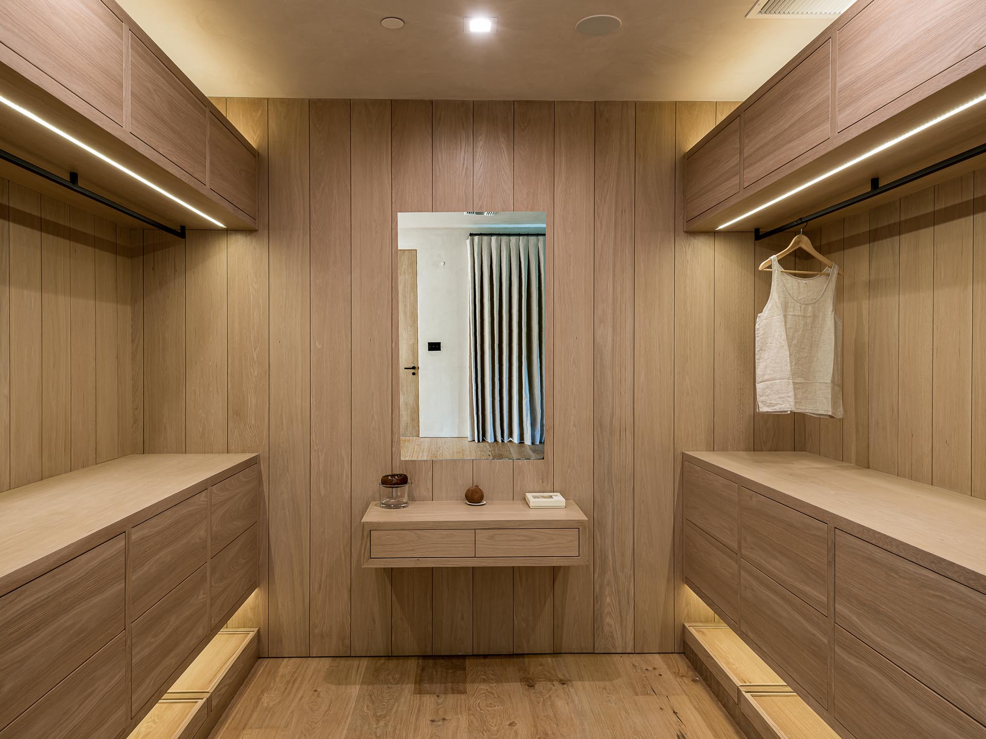 A walk-in closet lined with wood has a floating vanity.