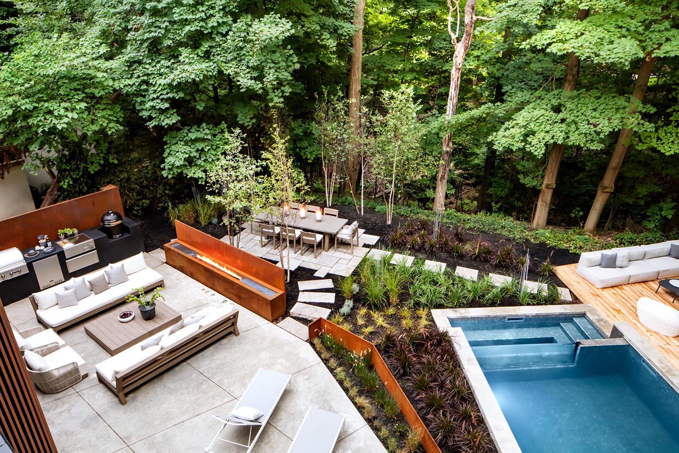 This modern outdoor space has been landscaped with a variety of different areas, including a swimming pool and deck, a lounge area with outdoor kitchen and fireplace, and a dining area.