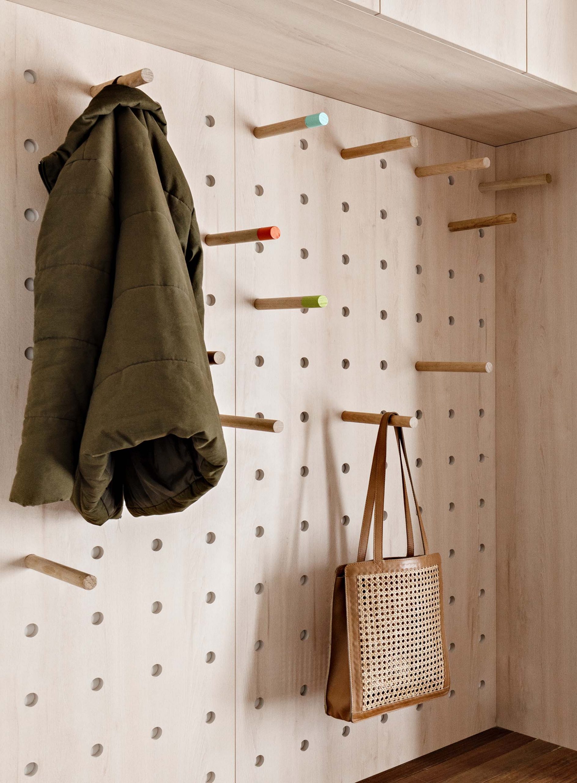 A modern mudroom / laundry room with minimalist wood cabinets, a wood bench, shoe storage, white countertop, and pegboard storage wall.