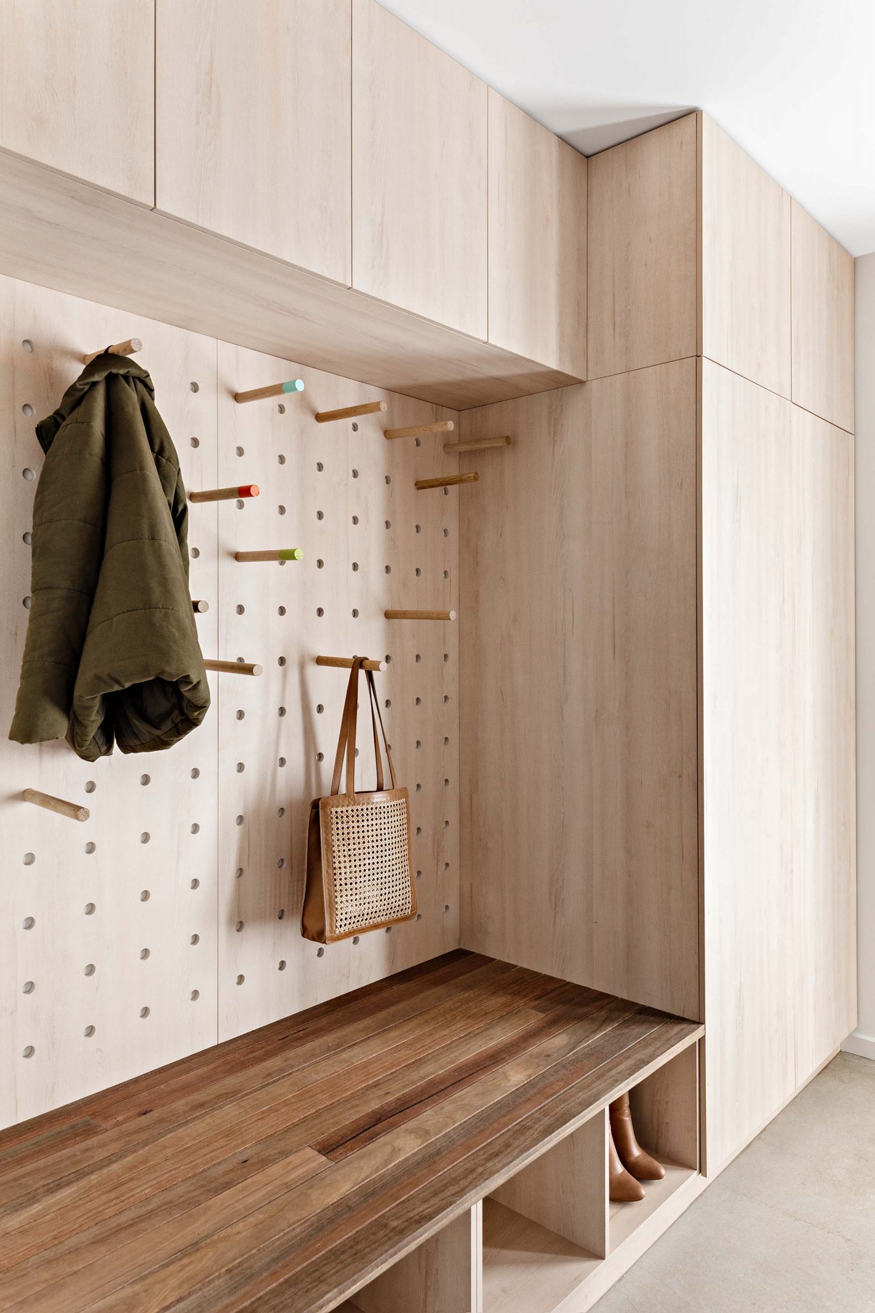 A modern mudroom / laundry room with minimalist wood cabinets, a wood bench, shoe storage, white countertop, and pegboard storage wall.