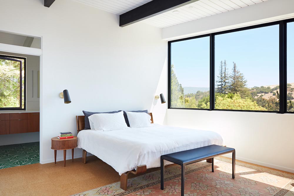 This remodeled primary bedroom has black accents, an en-suite bathroom, a small sitting area, and a desk tucked away into an alcove.