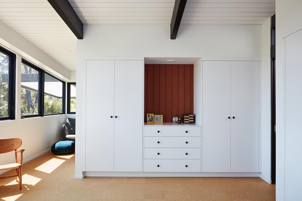 This remodeled primary bedroom has black accents, an en-suite bathroom, a small sitting area, and a desk tucked away into an alcove.