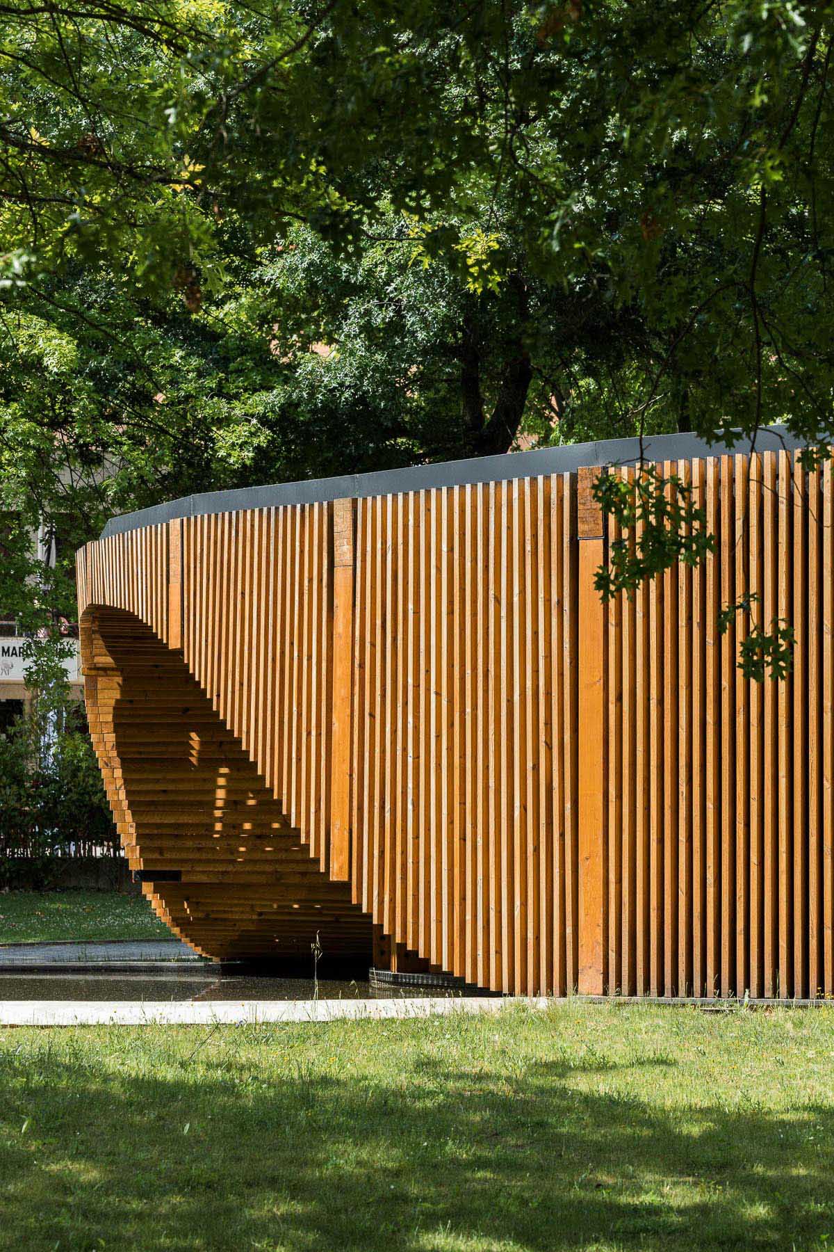 A small modern building has a circular design that's covered in vertical wood slats.