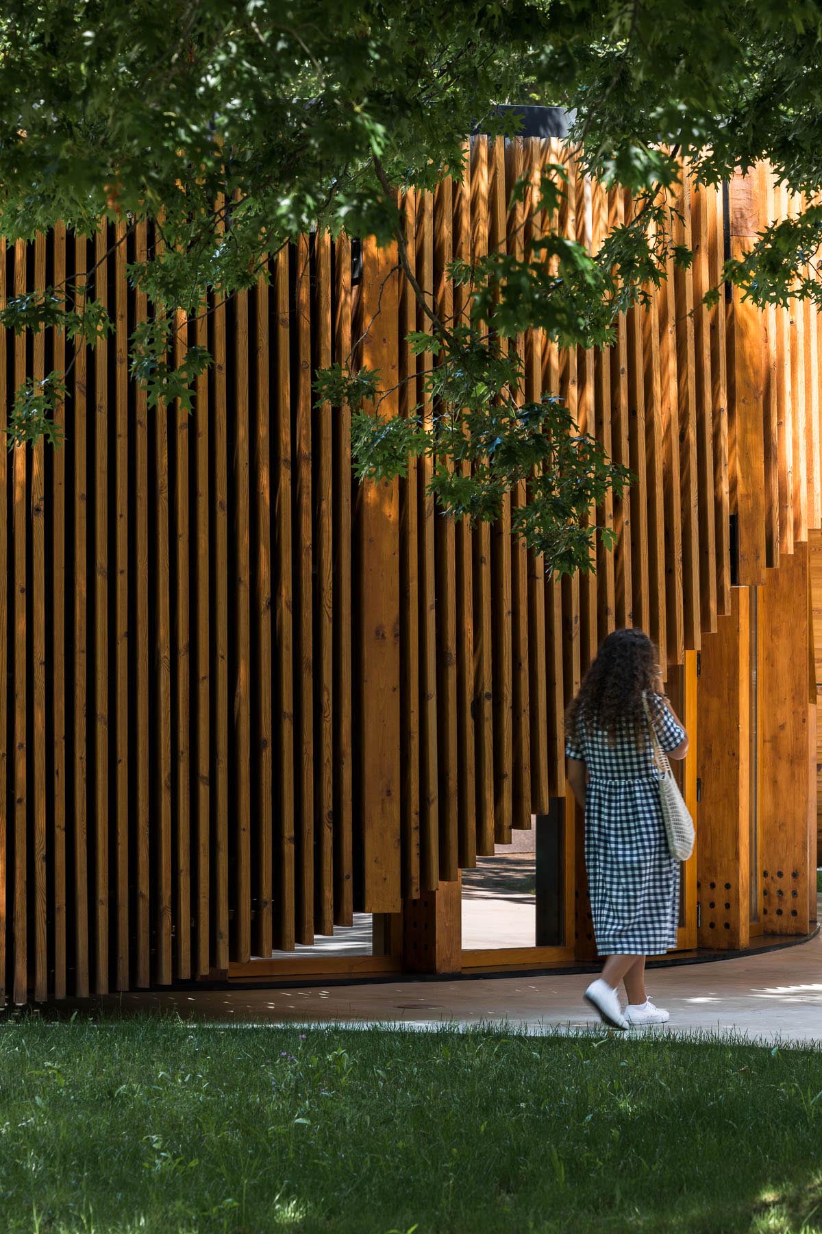 A small modern building has a circular design that's covered in vertical wood slats.